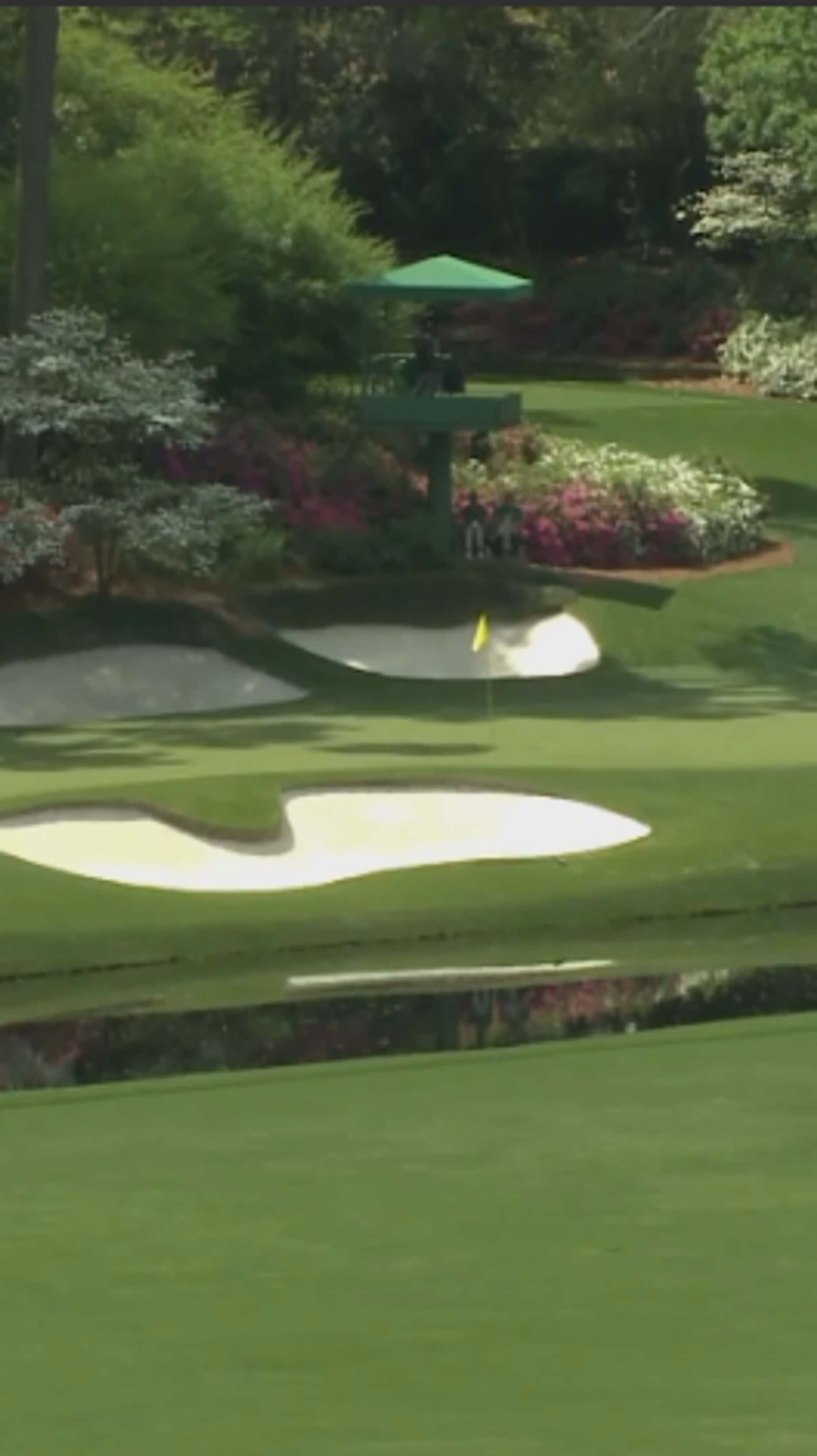 Augusta National iPhone 桌布 壁紙 — 在明亮的日光下，綠油油的高爾夫球場球道上有沙坑和色彩繽紛的花壇。