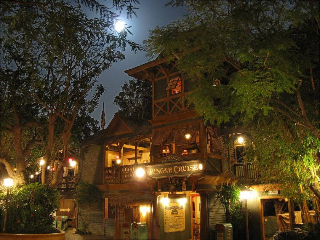 Jungle Cruise 桌布 壁紙 — 在明亮的滿月下，夜晚溫暖照明的叢林遊獵小屋，周圍環繞著茂密的樹木。