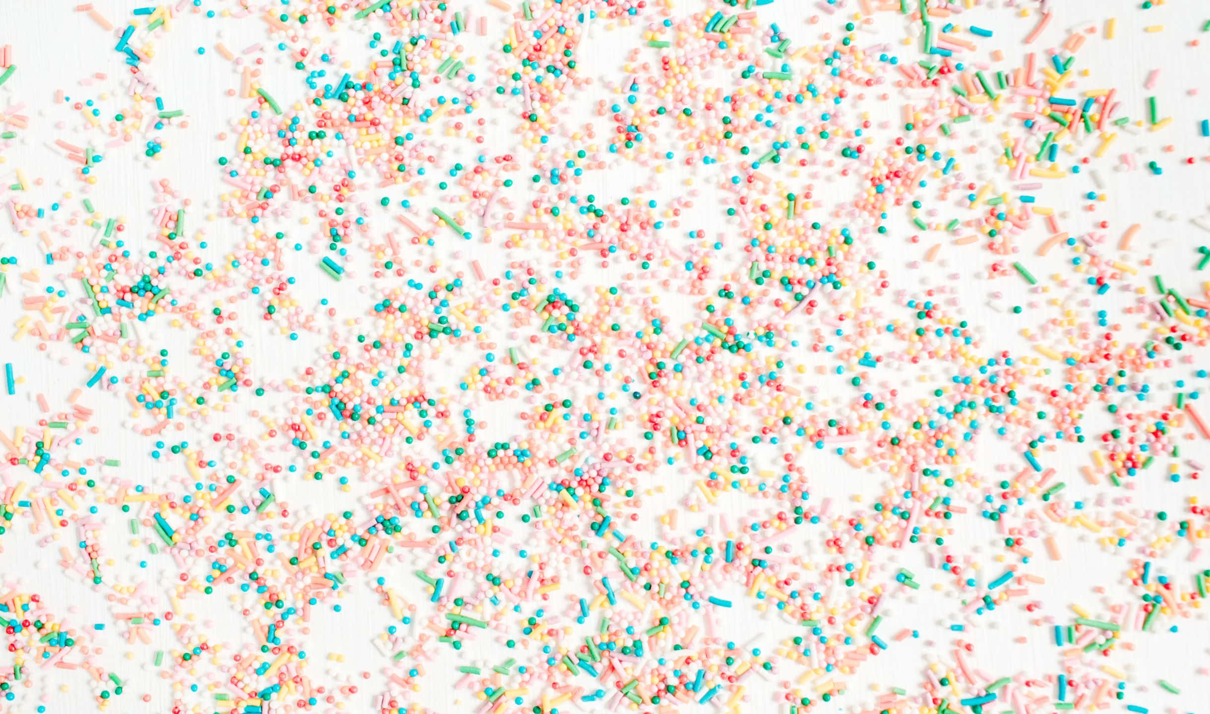 Sprinkles 桌布 壁紙 — 在明亮的白色表面上，散落著充滿活力的粉彩粉紅、綠色和黃色糖果灑。
