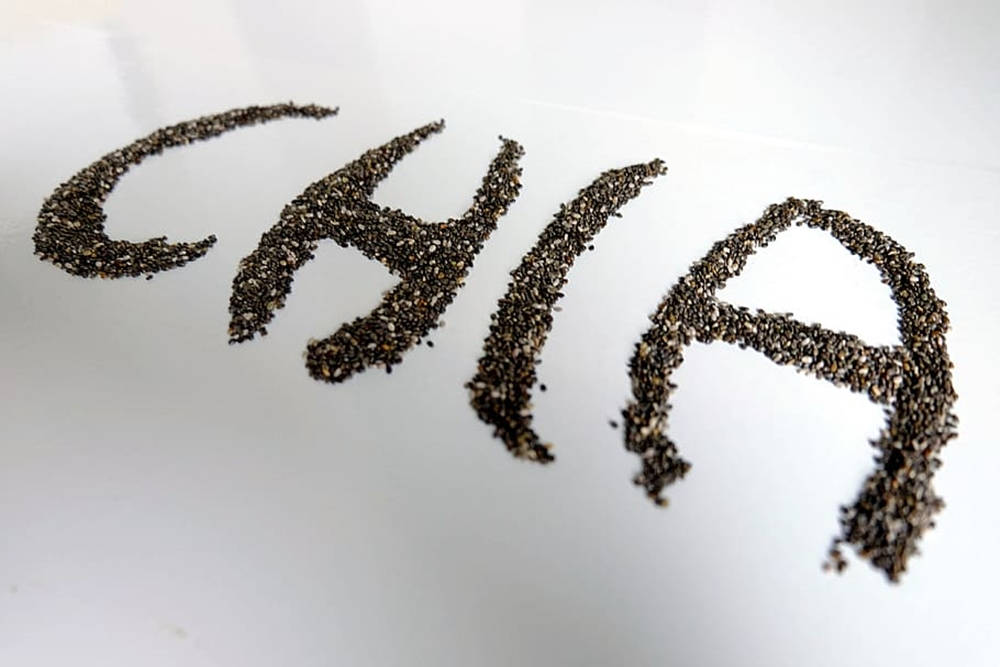 healthy 桌布 壁紙 — 在明亮的白色表面上用深色斑點奇亞籽拼出的「CHIA」這個字。