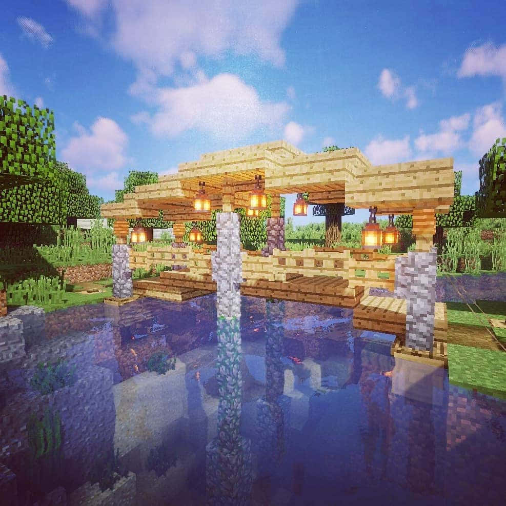 Minecraft Bridges 桌布 壁紙 — 在明亮的藍天下，Minecraft 森林中一條像素風格的木橋，掛著發光的燈籠，橫跨在倒映著景色的池塘上。