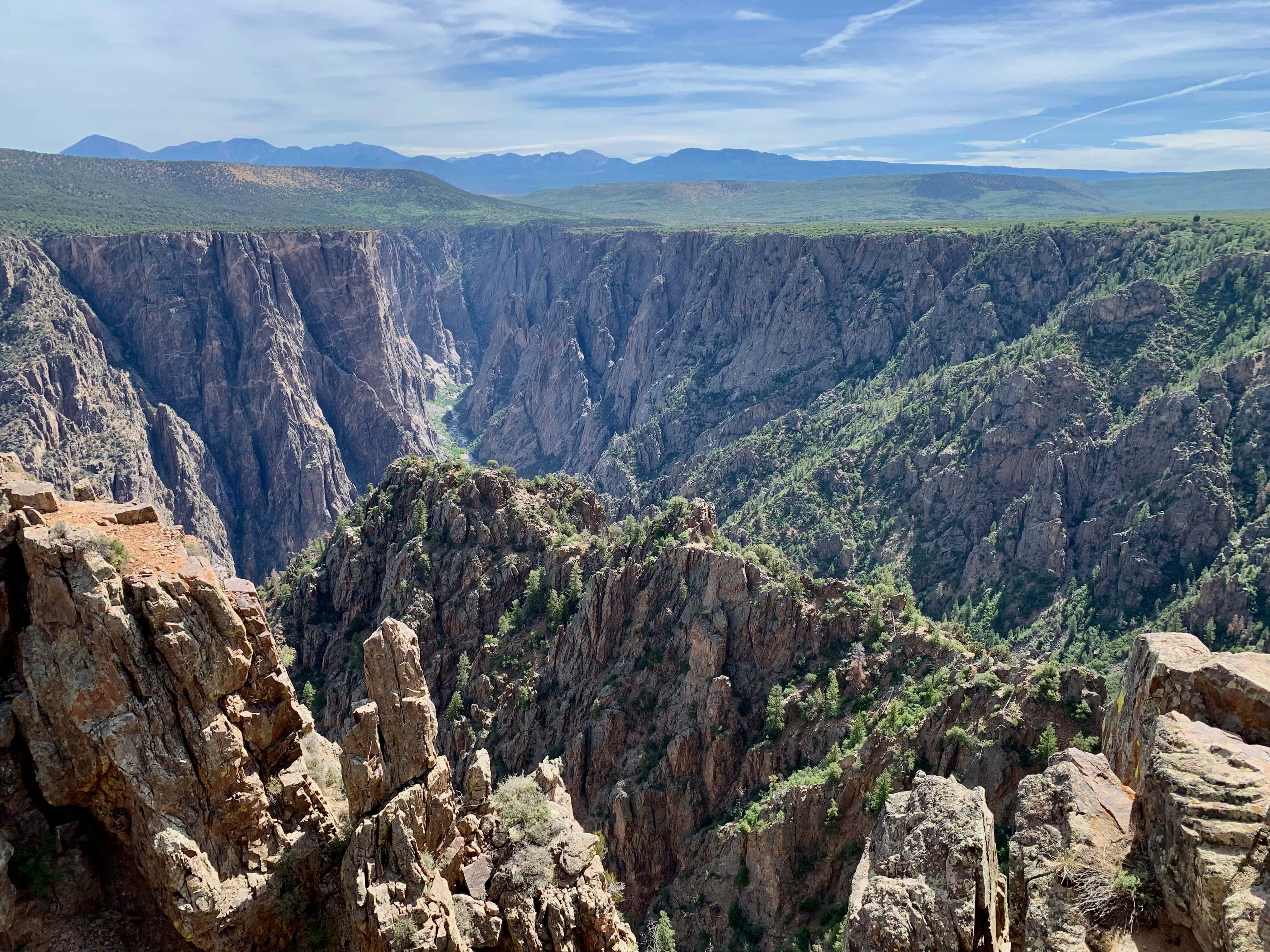 Black Canyon 桌布 壁紙 — 在明亮的藍天下，一個深峽谷的壯麗景色，有崎嶇懸崖和綠色植被。
