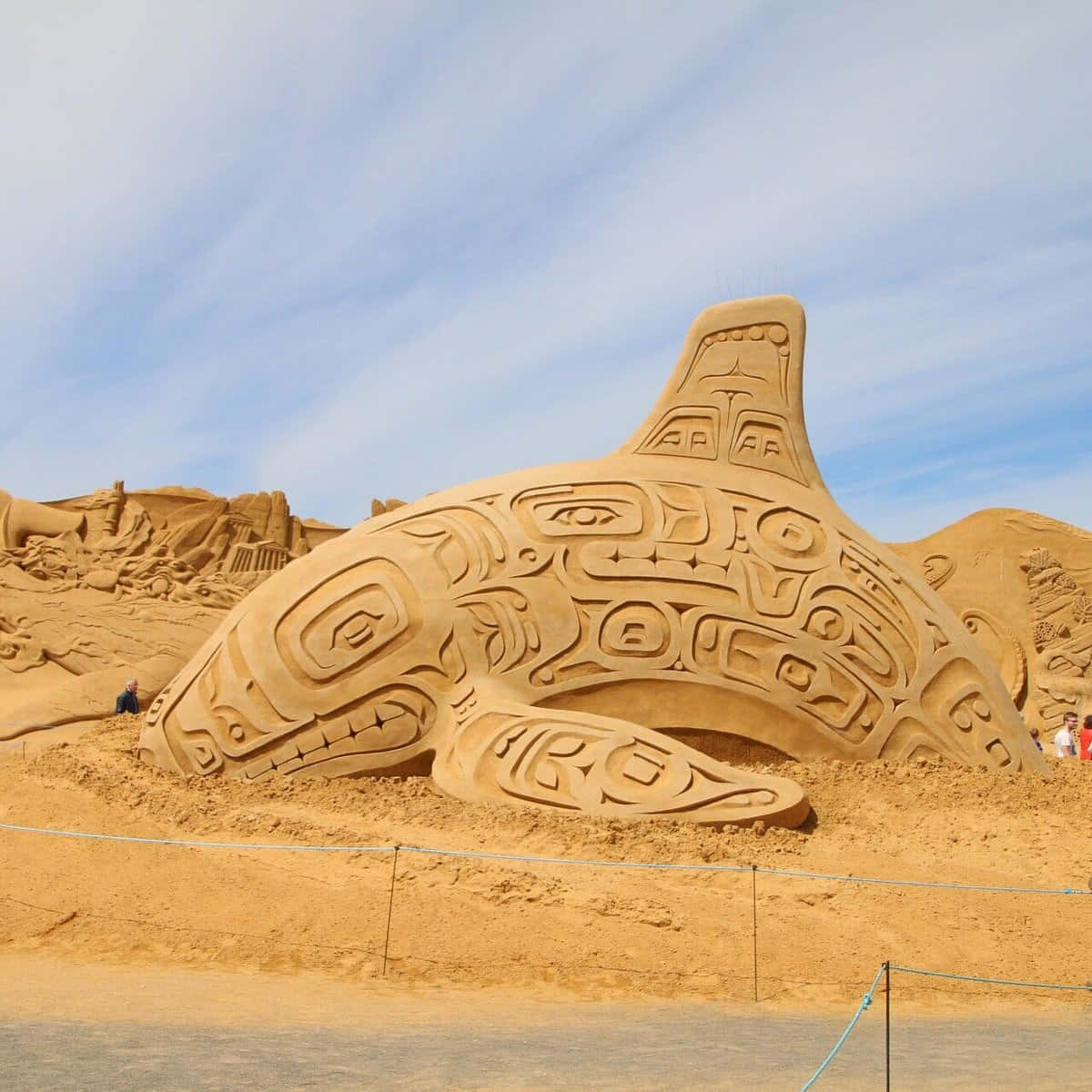 Sand Art 桌布 壁紙 — 在明亮的藍天下，一座裝飾著複雜部落圖案的巨大鯨魚沙雕。