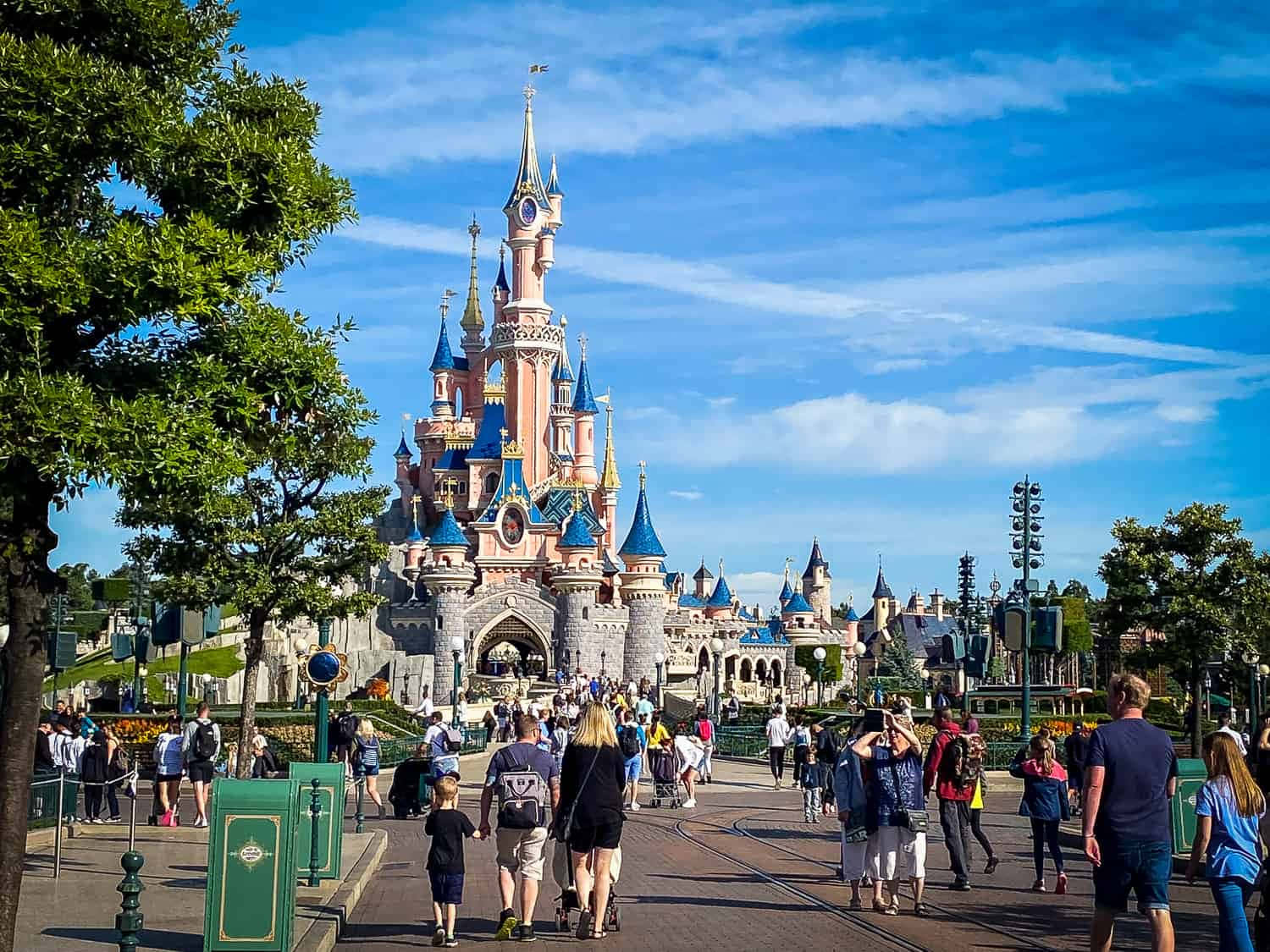 Disneyland Castle 桌布 壁紙 — 在明亮的藍天下，人群走向迪士尼樂園巴黎城堡的充滿活力的白天照片。