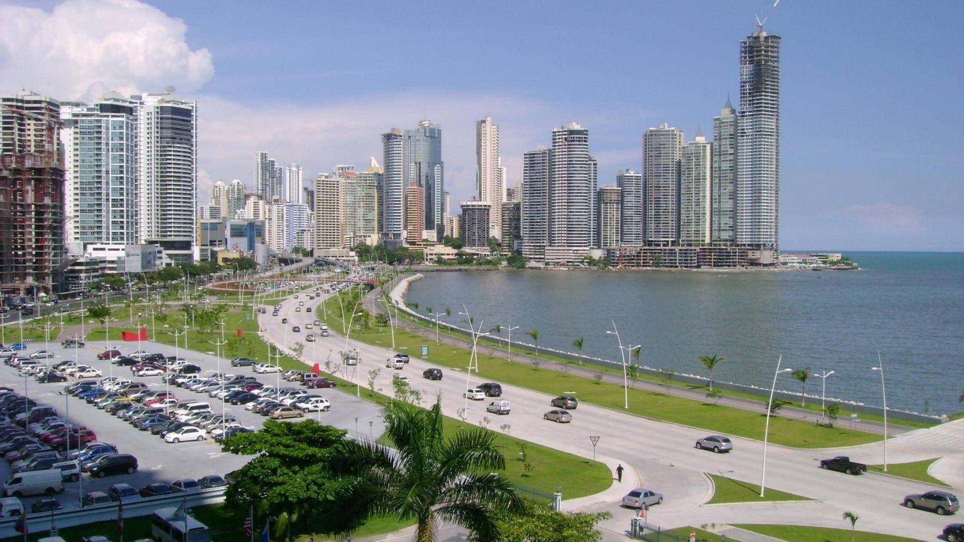 View 桌布 壁紙 — 在明亮的藍天下，現代摩天大樓沿著彎曲的海濱道路排列，形成充滿活力的沿海城市景觀。