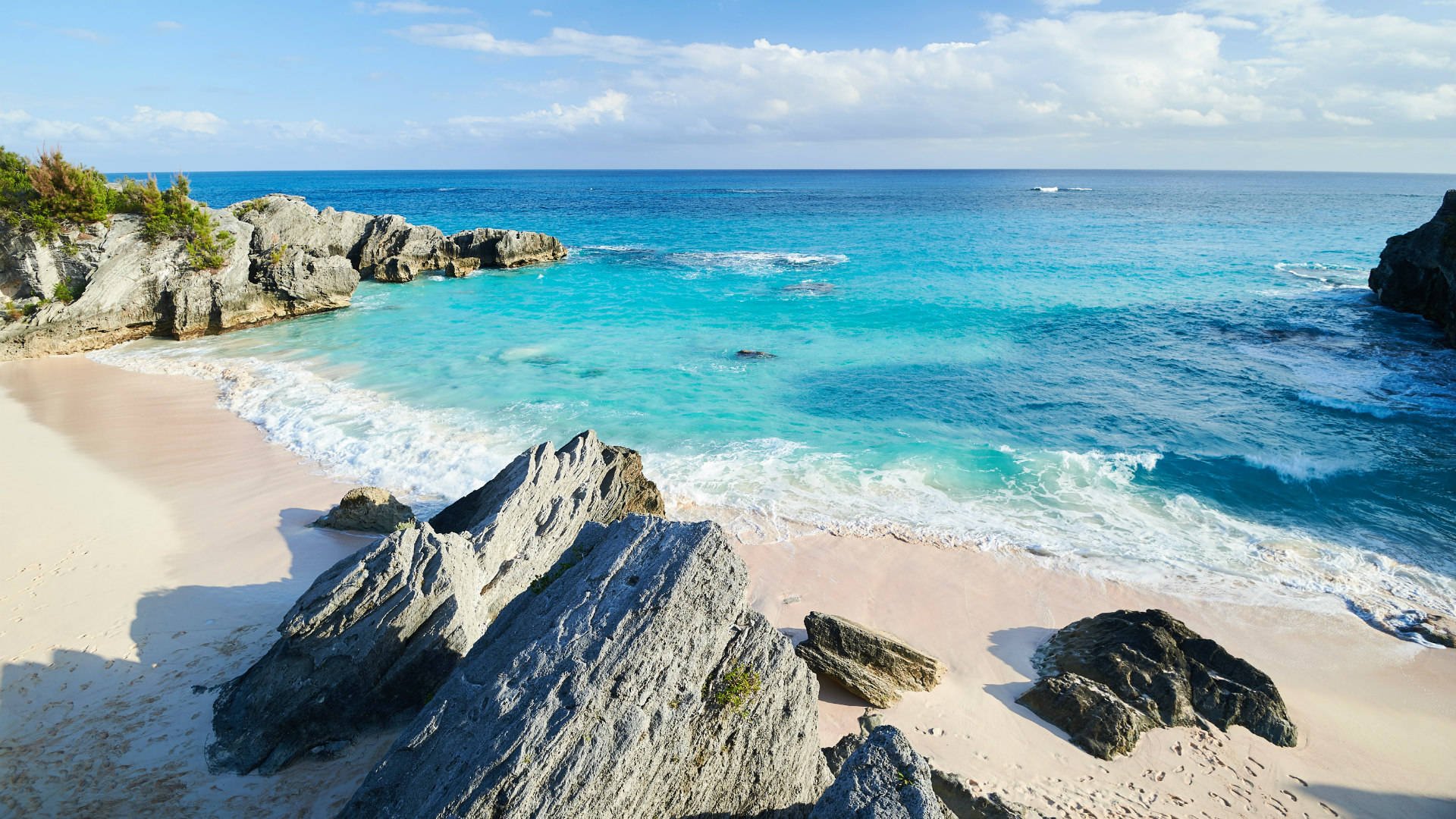 Bermuda 桌布 壁紙 — 在明亮的藍天下，碧綠的海浪拍打著由粗糙灰色岩石環繞的粉紅色沙灘。