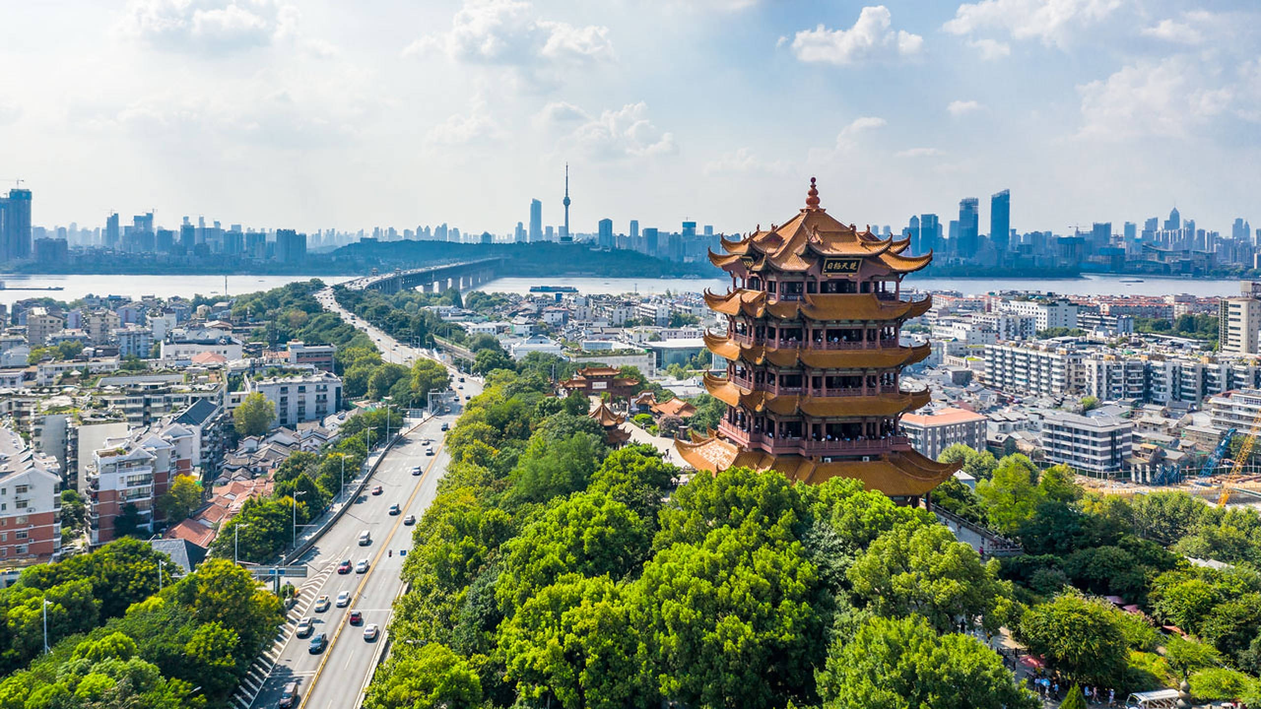 Wuhan 桌布 壁紙 — 在明亮的藍天下，繁華的現代城市景觀中，被茂密綠樹環繞的傳統中國寶塔的航拍視圖。