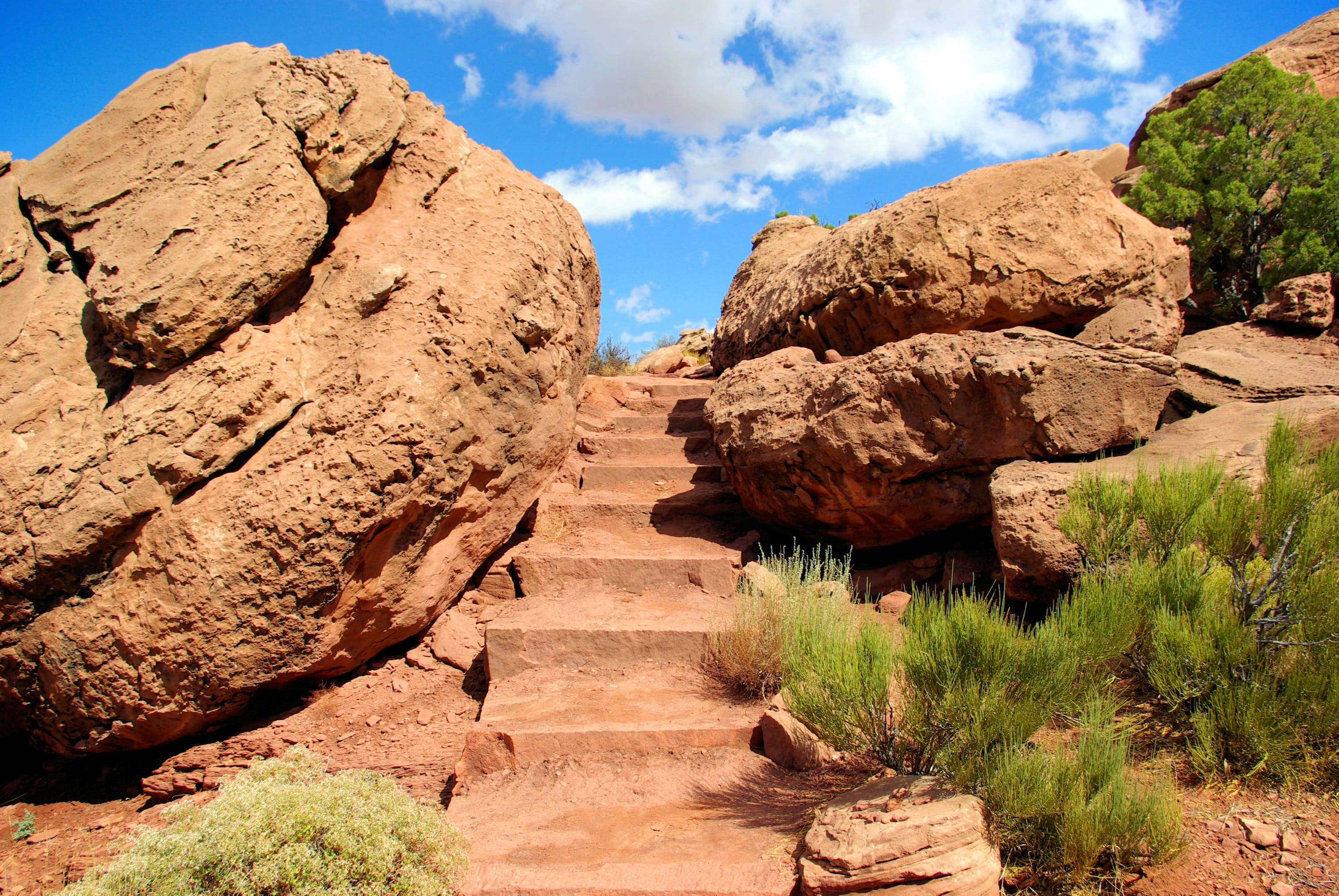 Canyonlands National Park 桌布 壁紙 — 在明亮的藍天和蓬鬆白雲下，一條陽光普照的樓梯雕刻在紅色岩層中。