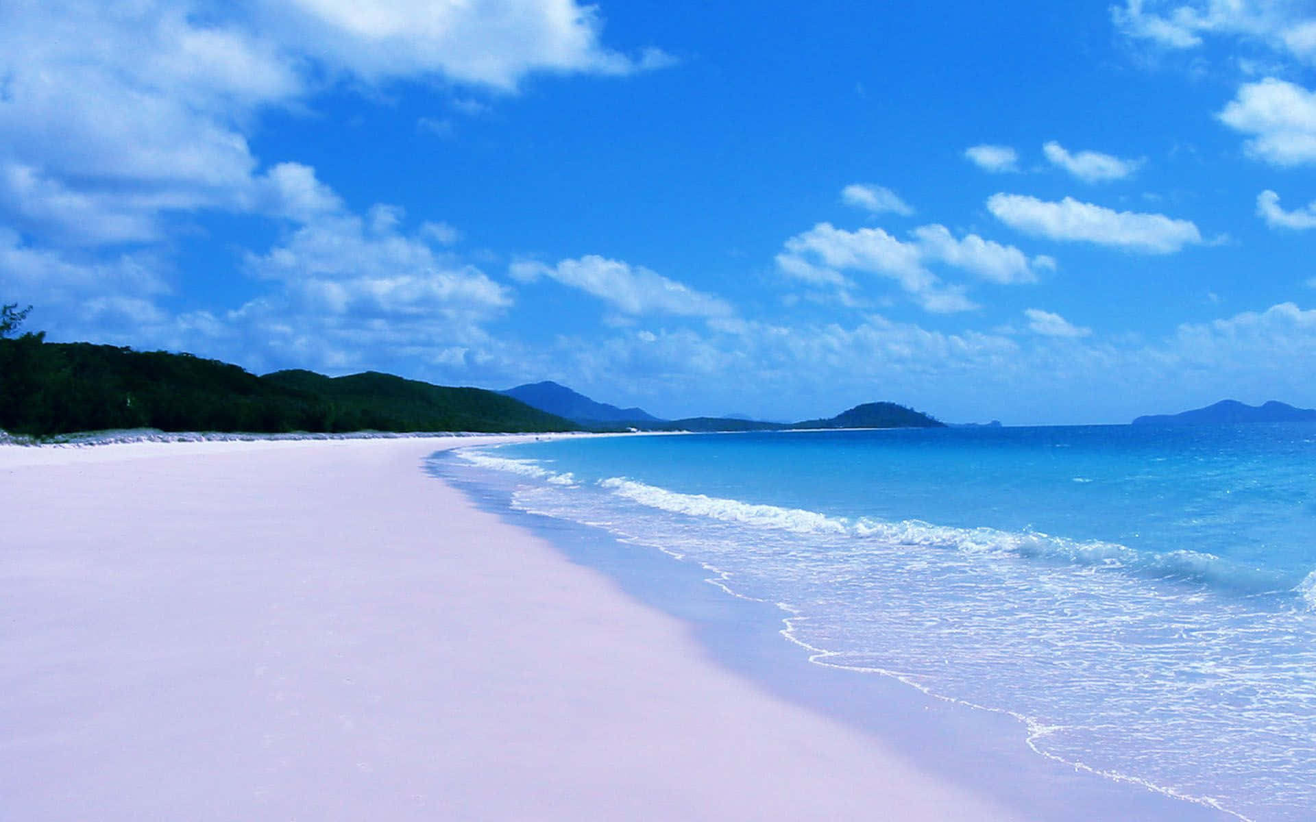 Australia Beach 桌布 壁紙 — 在明亮的藍天和蓬鬆的雲朵下，粉紅沙灘、碧綠海水和鬱鬱蔥蔥的綠色山丘的壯麗景色。