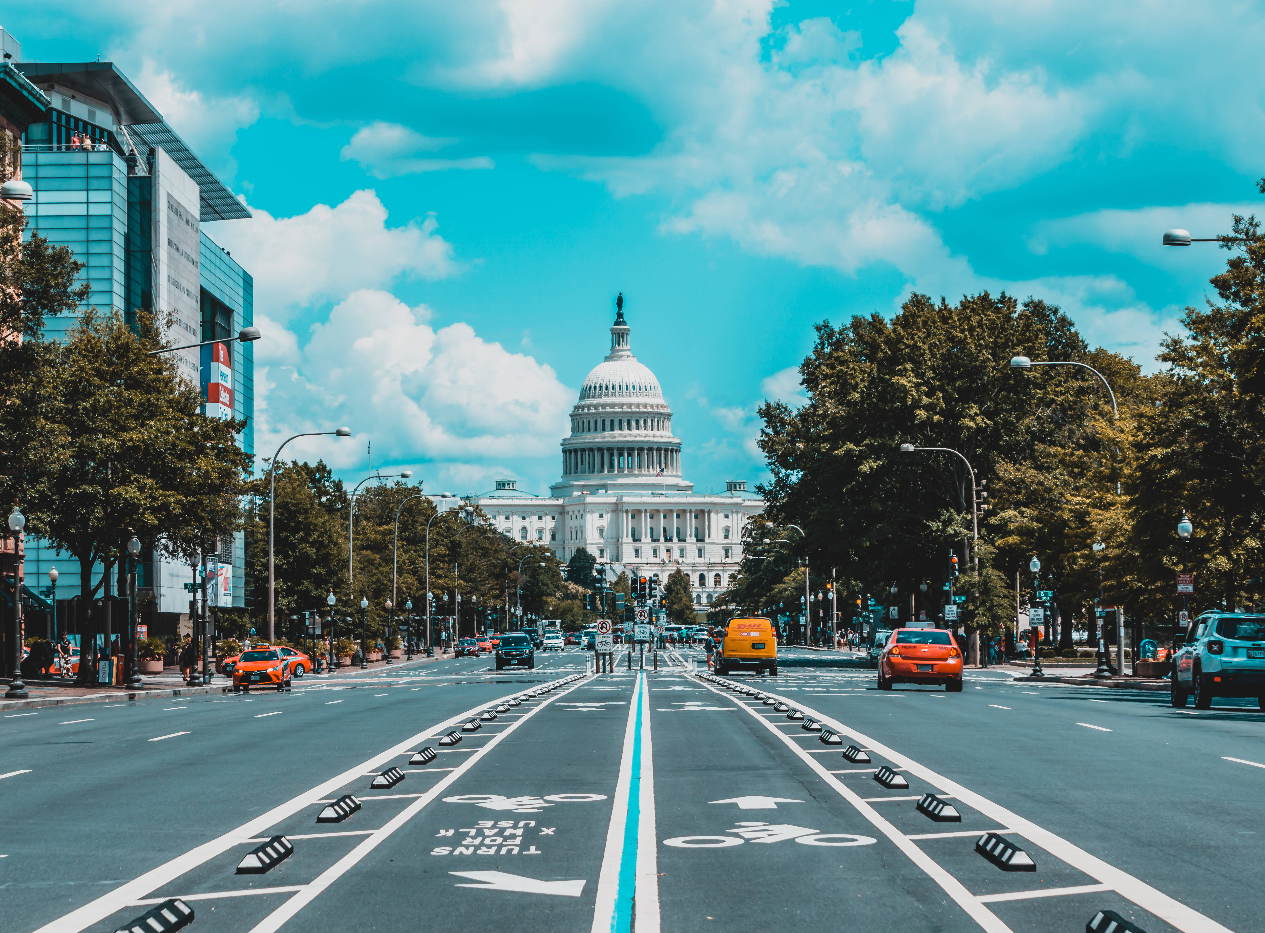 Washington 桌布 壁紙 — 在明亮的藍天和蓬鬆雲朵下，沿著寬闊的城市街道望向標誌性的美國國會大廈的充滿活力的日間景色。