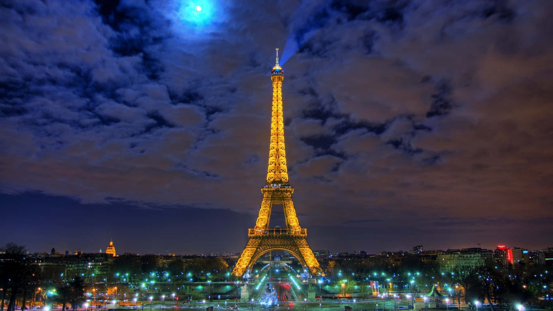 Eiffel Tower 桌布 壁紙 — 在明亮的藍月和漩渦雲彩的戲劇性夜空下，艾菲爾鐵塔閃耀著金色光芒。