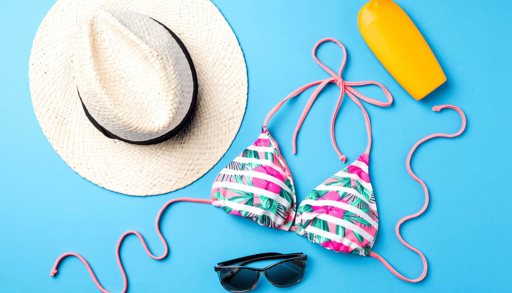 Beach Accessories 桌布 壁紙 — 在明亮的藍色背景上，以鮮豔的平鋪方式展示夏季必需品，包括草帽、比基尼、太陽眼鏡和防曬乳。