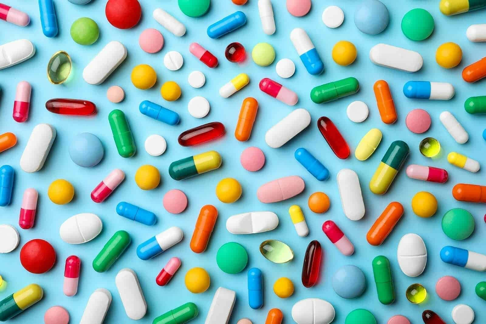 pills 桌布 壁紙 — 在明亮的藍色背景上，散落著色彩繽紛的藥丸和膠囊，充滿活力。
