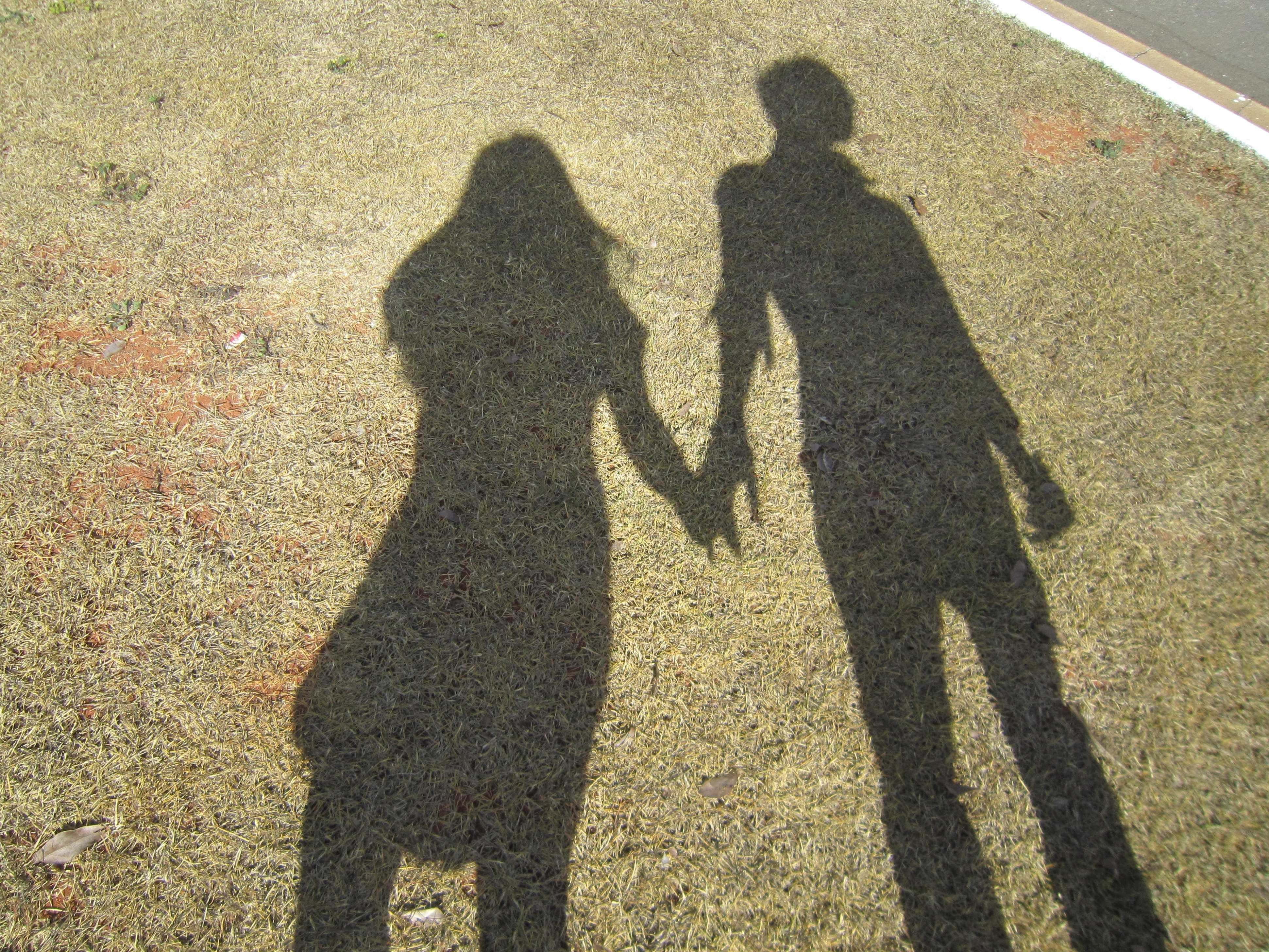 Couple Holding Hand 桌布 壁紙 — 在明亮的陽光下，兩個人牽手的剪影在乾草上投下長長的影子。