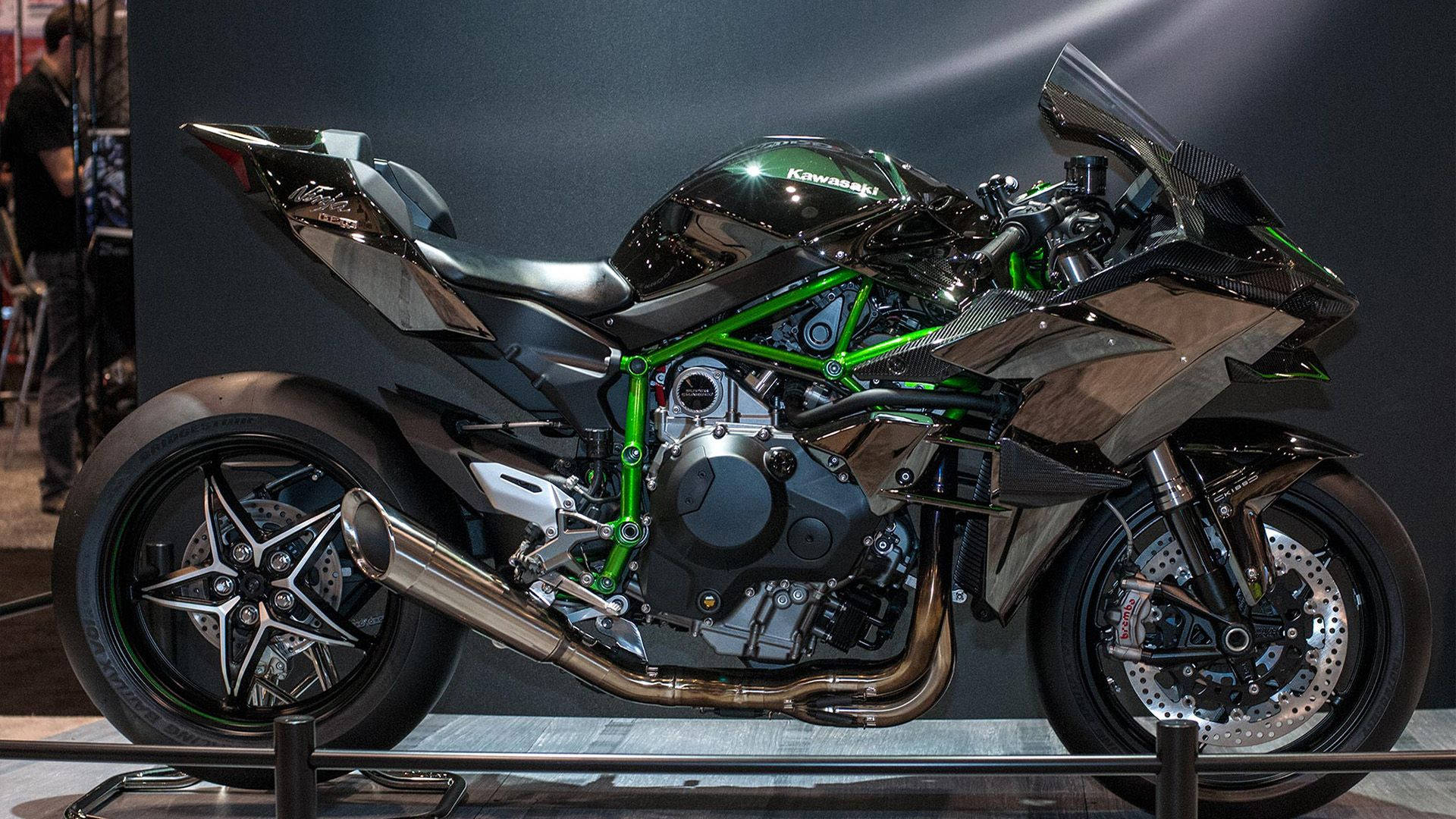 機車 桌布 壁紙 — 在明亮聚光燈下，一輛時尚的黑色和綠色 Kawasaki 運動型摩托車，帶有外露引擎和碳纖維細節。