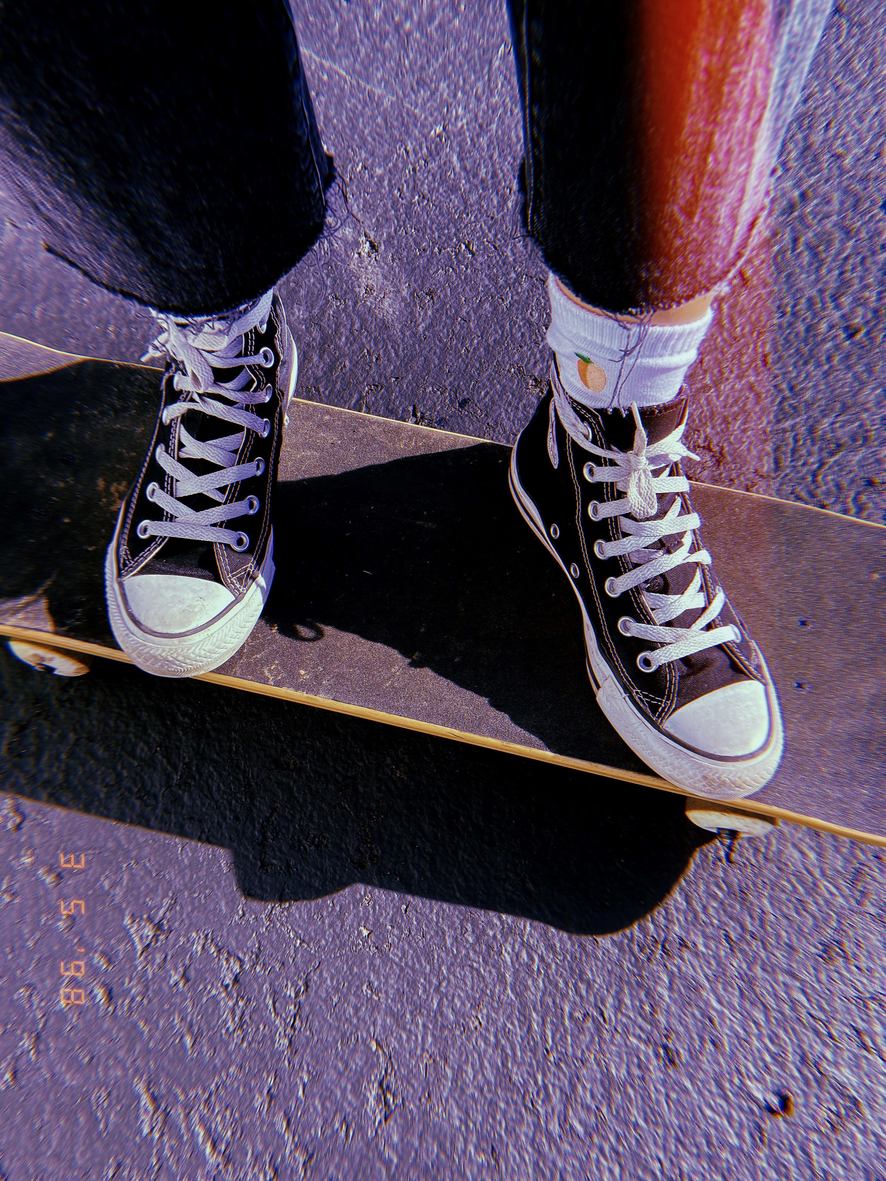 Skater Girl Aesthetic 桌布 壁紙 — 在明亮陽光下，紫色紋理路面上的滑板上，白色鞋帶和鞋底黑色高筒運動鞋的特寫。