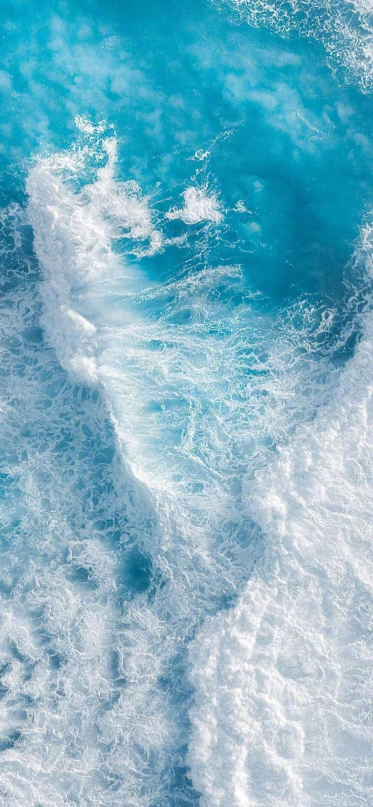 在明亮陽光下，綠松石色海洋波浪與白色泡沫撞擊。 — iPhone 14 壁紙