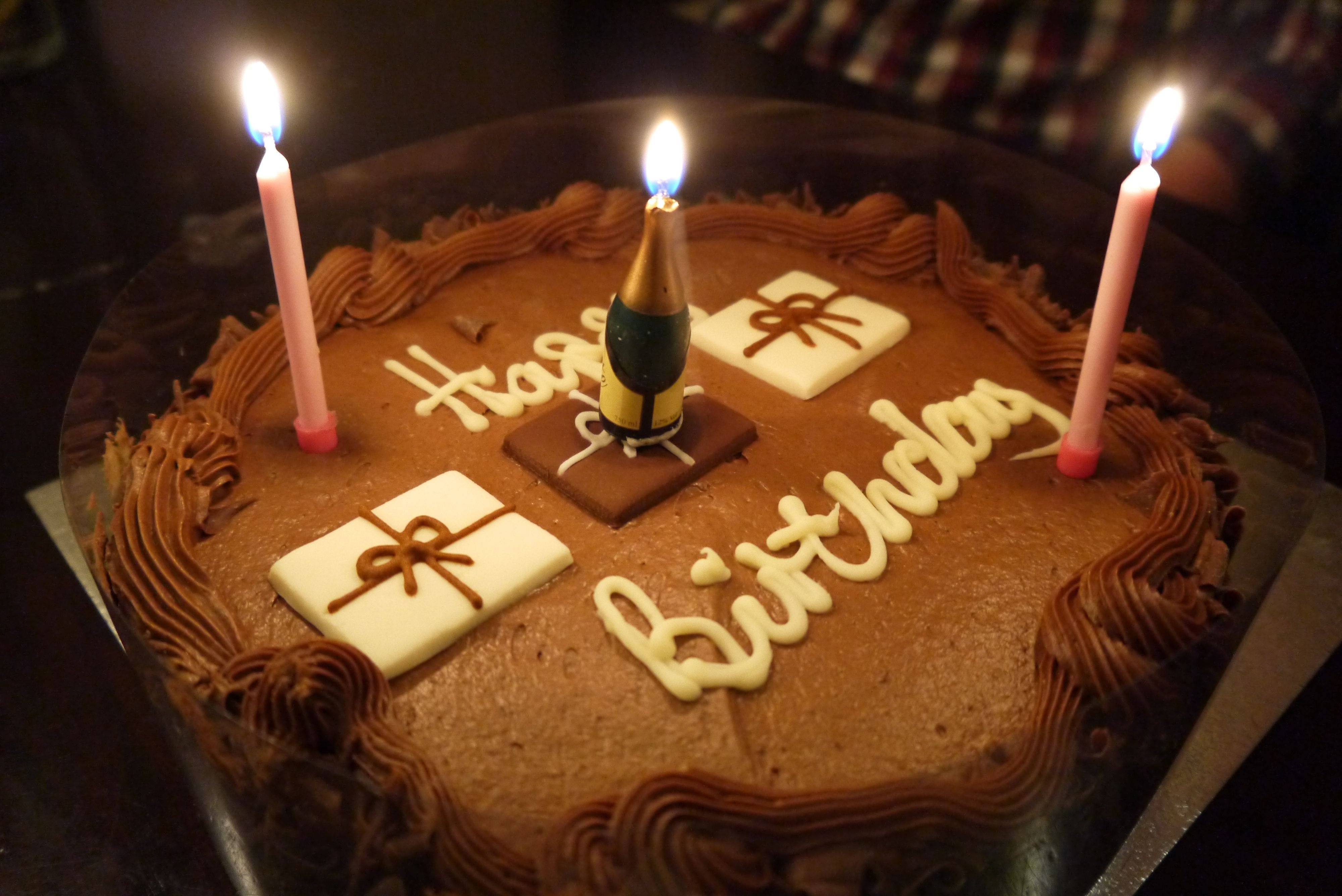 蛋糕 桌布 壁紙 — 在昏暗燈光下，一個帶有燃點蠟燭和「Happy Birthday」糖霜的巧克力生日蛋糕。
