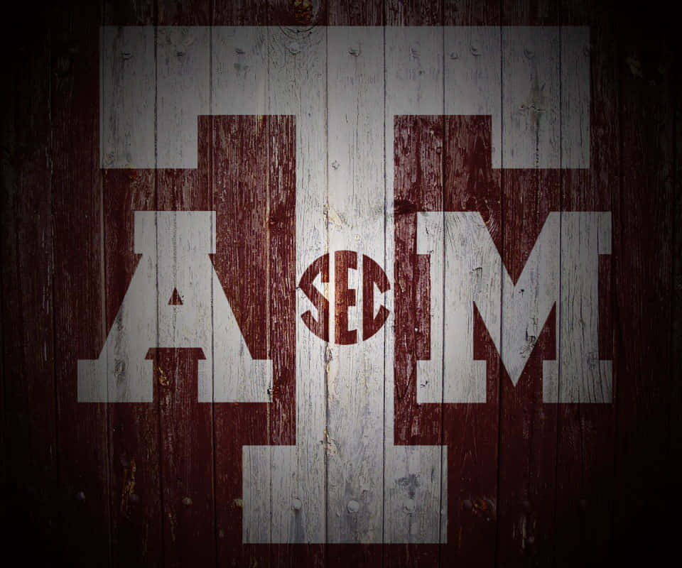 Texas Am 桌布 壁紙 — 在昏暗燈光下，風化木板上繪有大型白色和栗色 Texas A&M 字母及 SEC 標誌。