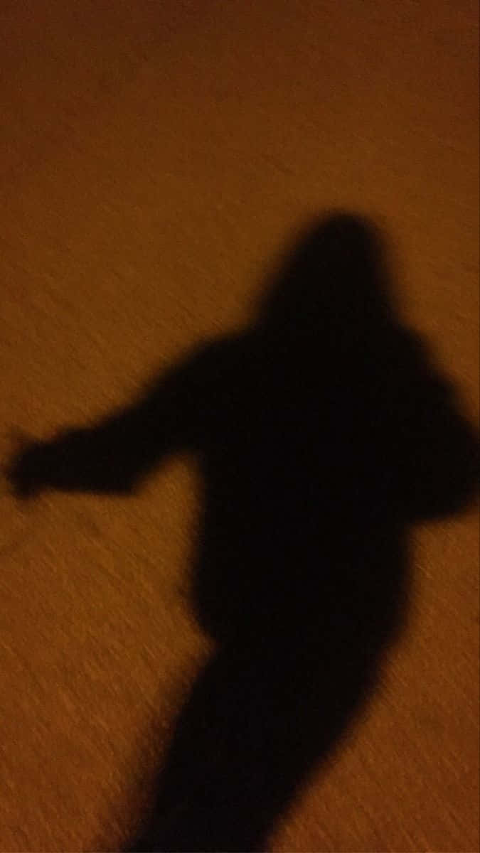 shadow 桌布 壁紙 — 在昏暗的人造燈光下，一個深色的人影伸展在帶紋理的橙色牆壁上。