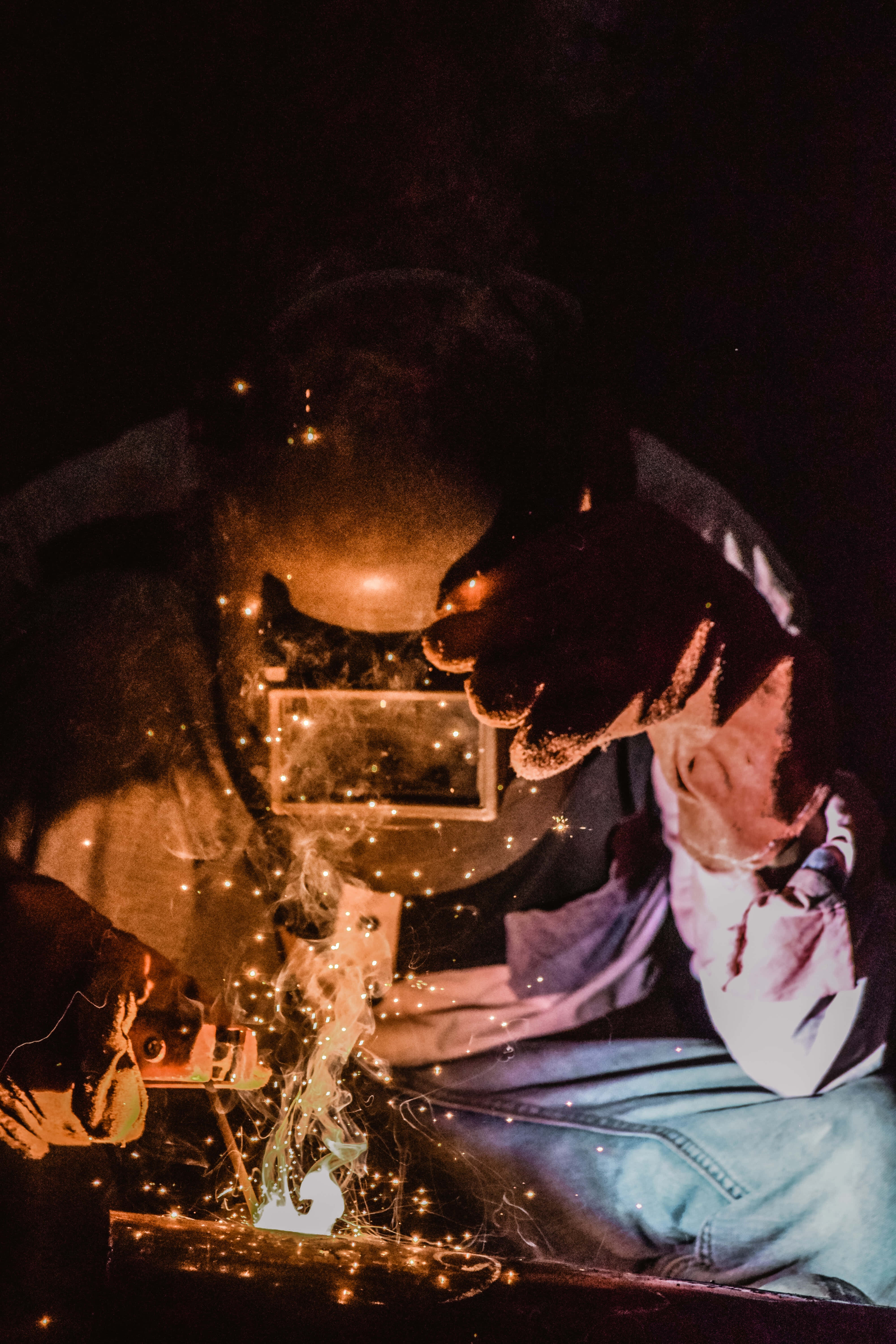 welding 桌布 壁紙 — 在昏暗的工作坊中，一名焊工戴著防護面罩和手套，產生明亮的金色火花。