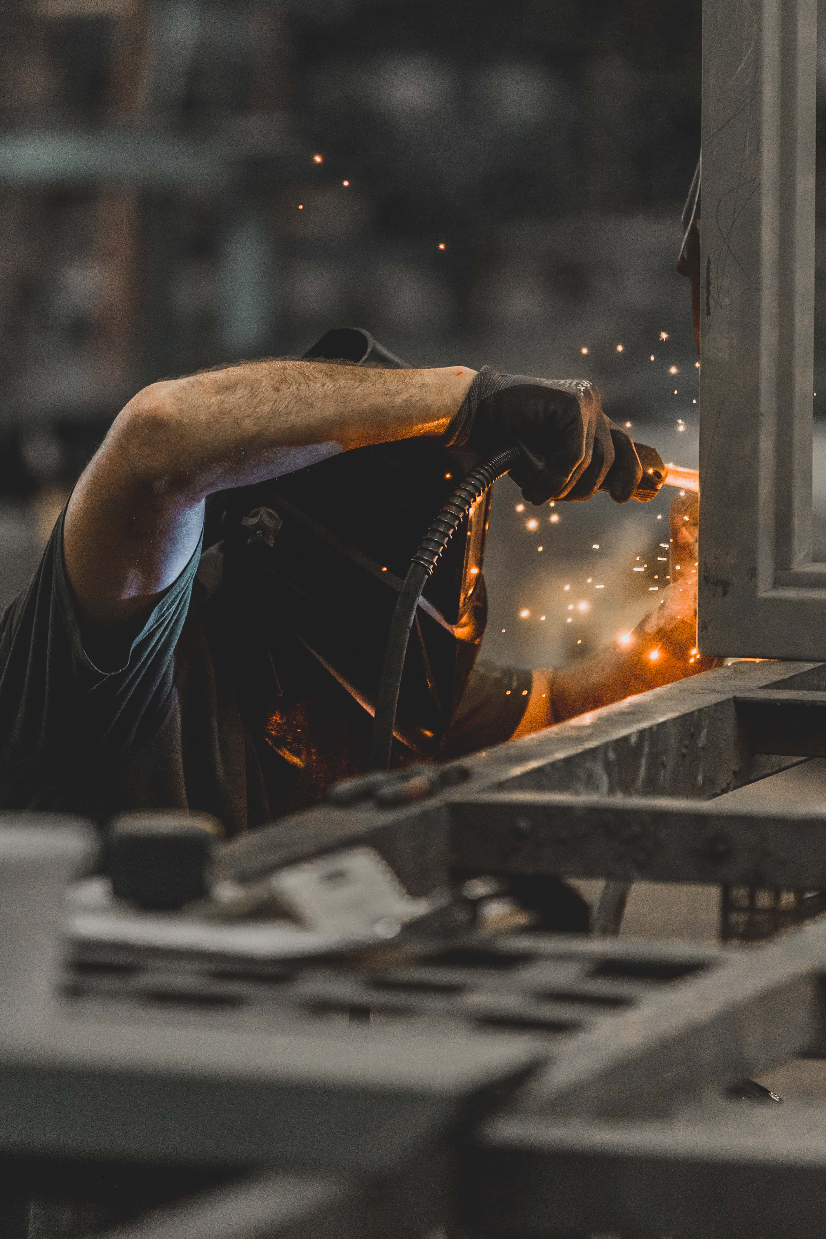 Working 桌布 壁紙 — 在昏暗的工業工場中，焊工戴著手套的手在熔接金屬時發出明亮火花。
