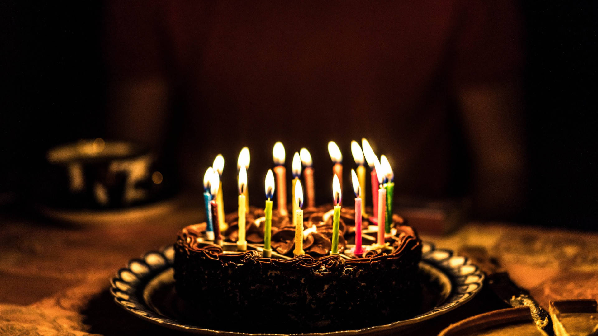 my 桌布 壁紙 — 在昏暗的房間裡，一個巧克力生日蛋糕上插著色彩繽紛的點燃蠟燭，溫暖地閃耀著。
