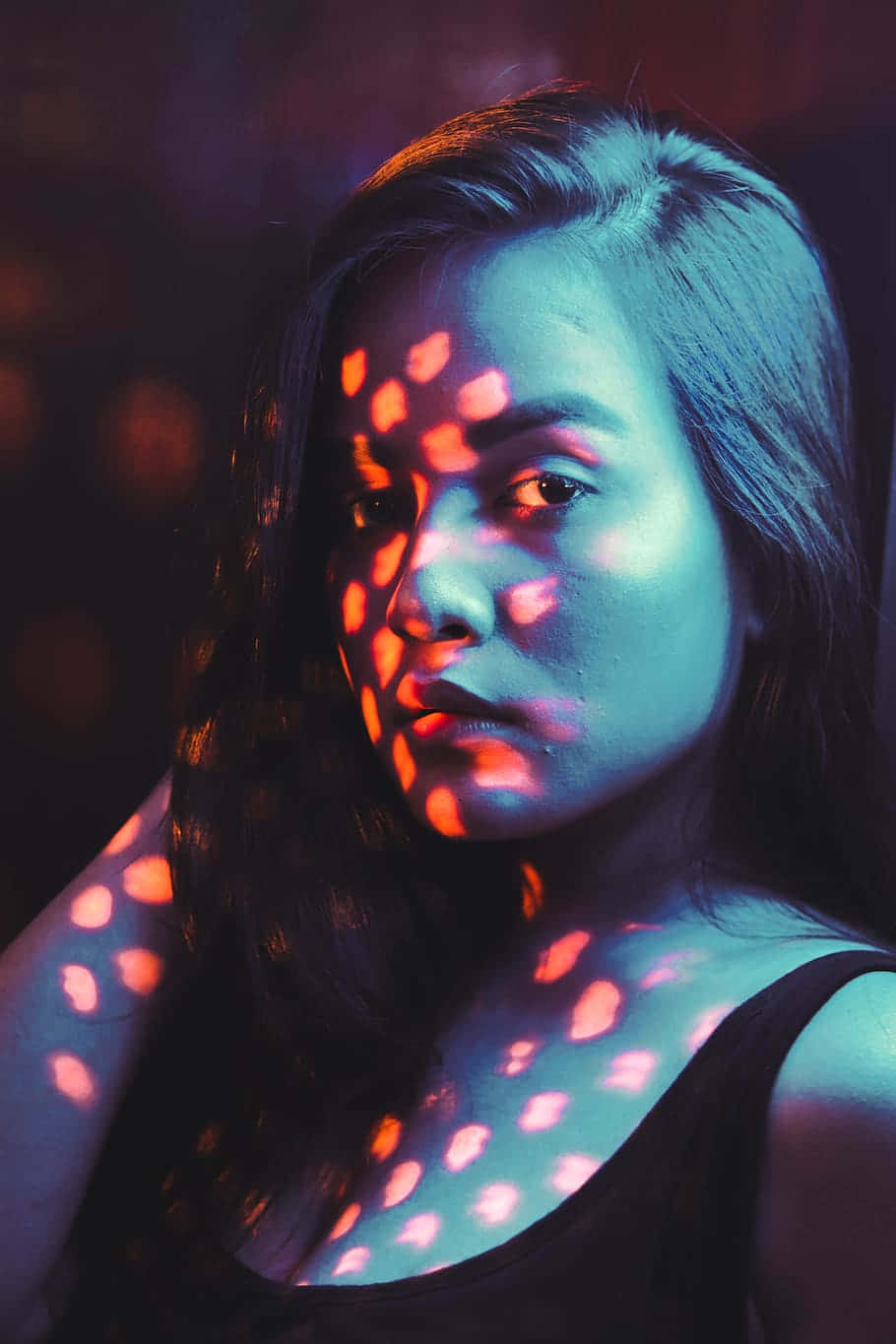 Tumblr Photography 桌布 壁紙 — 在昏暗的環境中，一位女性的臉部和肩膀被鮮豔的藍色和橙色光圖案照亮。