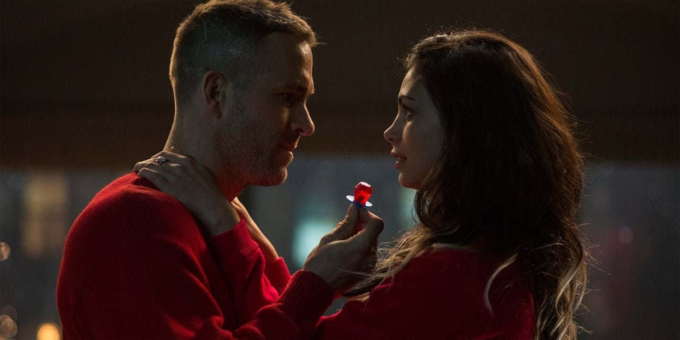 Deadpool And Vanessa 桌布 壁紙 — 在昏暗的環境中，一名穿著紅色毛衣的男子和一名穿著紅色毛衣的女子分享親密時刻，她將紅色棒棒糖靠近他的嘴唇。