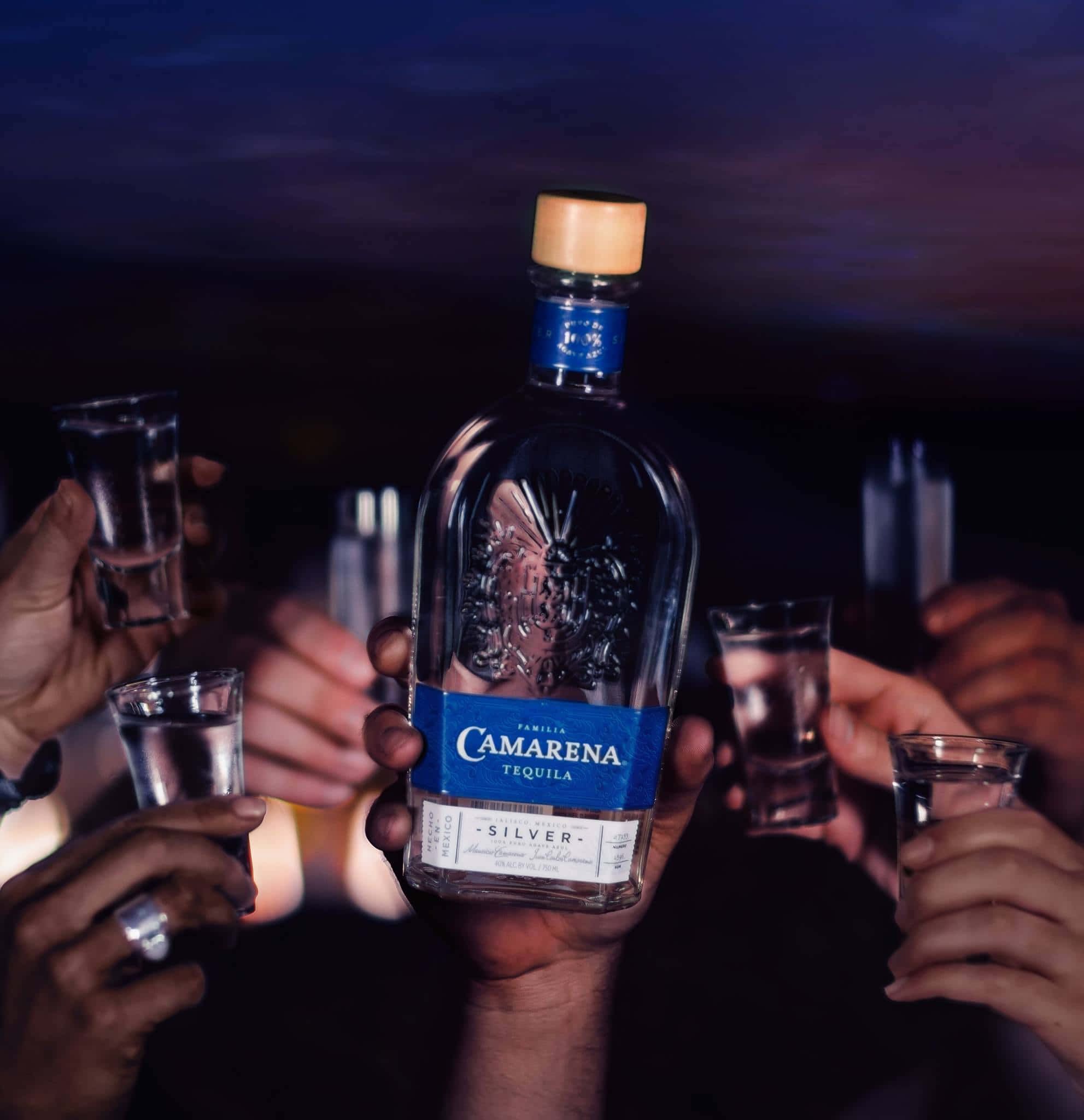 Tequila 桌布 壁紙 — 在昏暗的社交聚會中，手舉起一瓶Camarena Silver Tequila和烈酒杯。