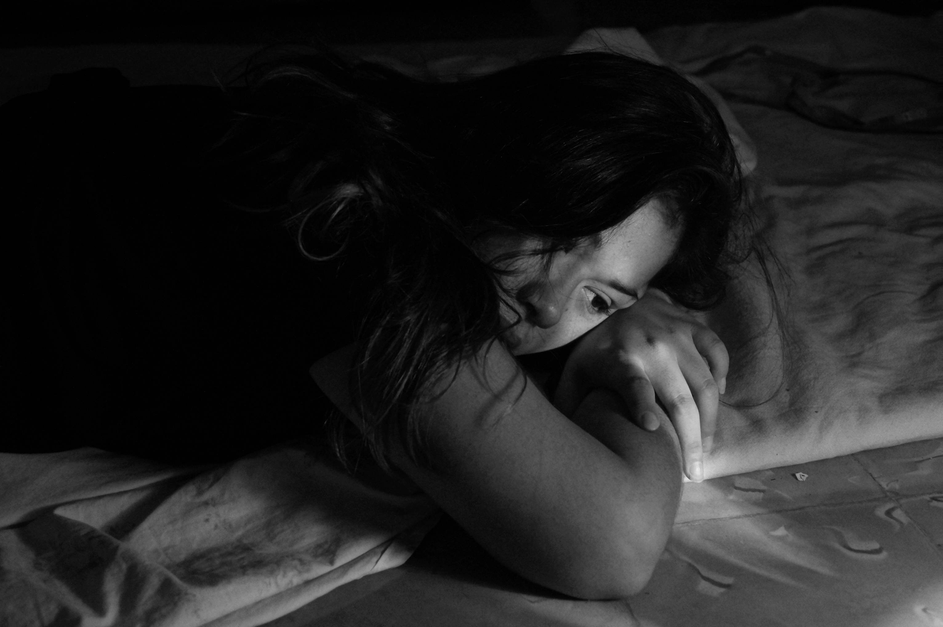 Sad Alone 桌布 壁紙 — 在昏暗的黑白場景中，一位女士將頭靠在手臂上，躺在床上，傳達出安靜的內省。