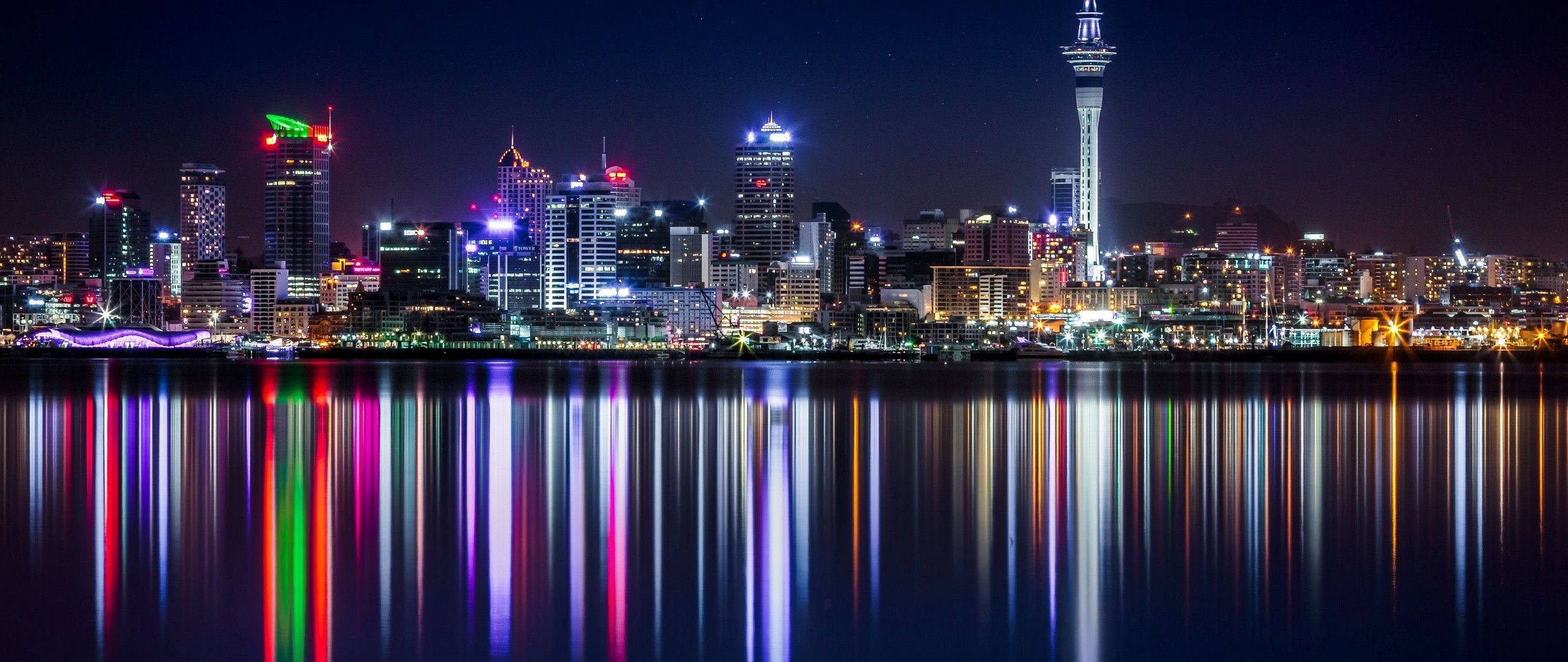城市風景 桌布 壁紙 — 在星空下，璀璨的夜間城市天際線，鮮豔的霓虹燈完美地倒映在平靜的水面上。