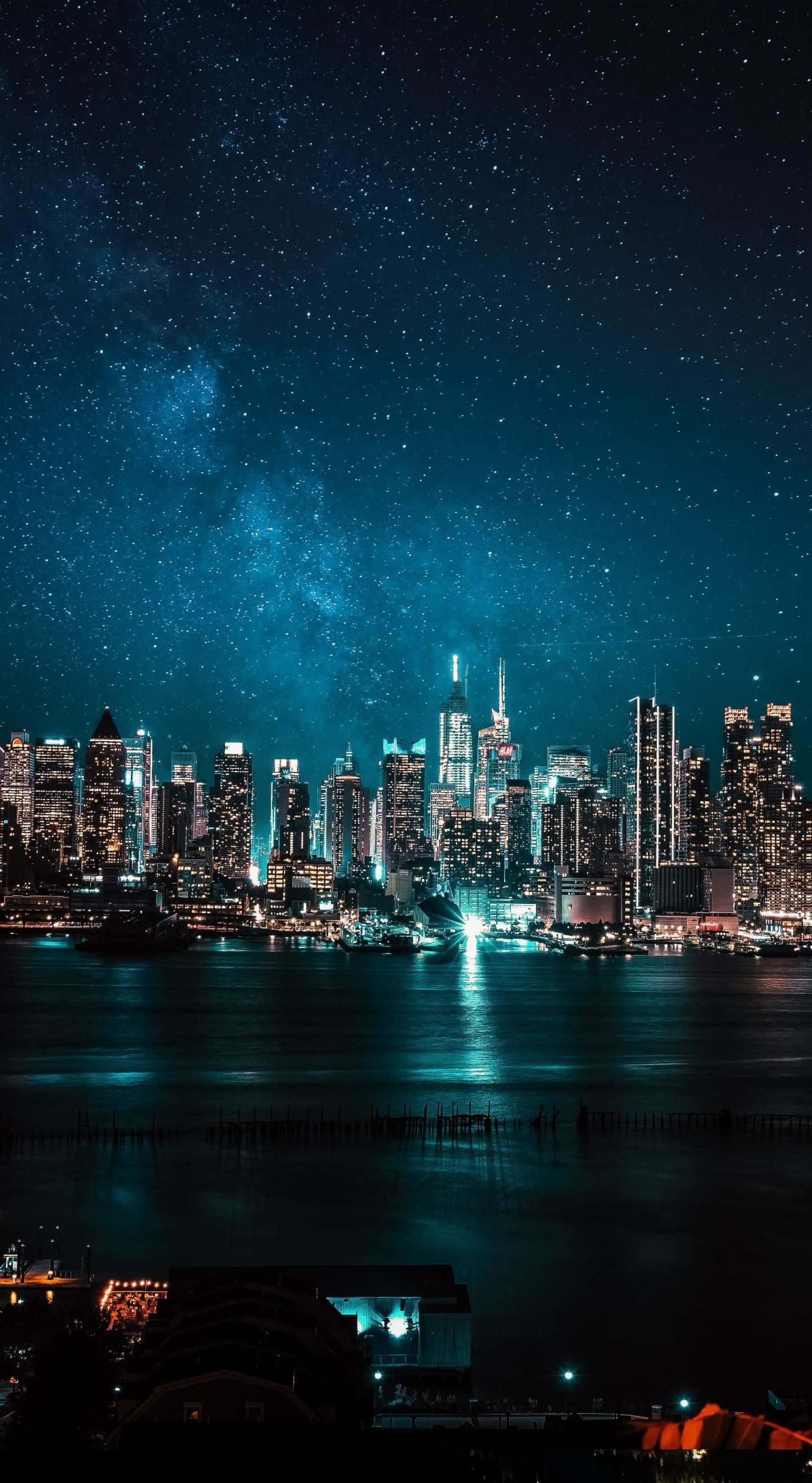 城市風景 桌布 壁紙 — 在星空下，銀河在水面上閃耀，令人目眩神迷的城市天際線夜景。