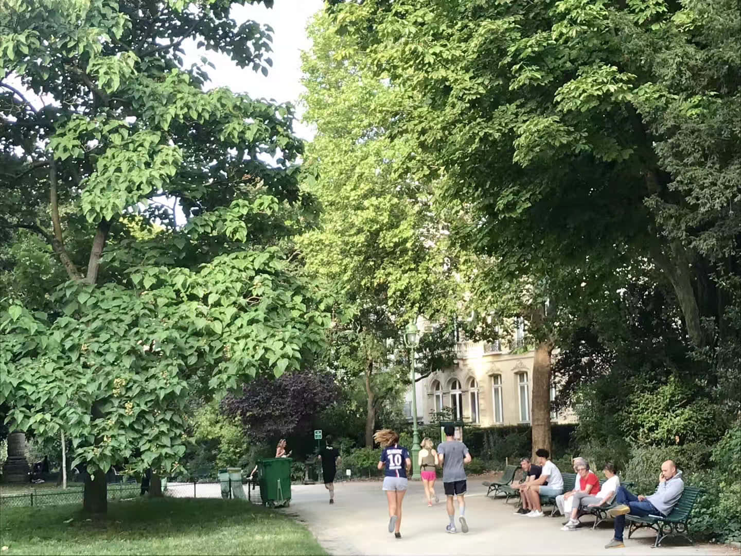 公園 桌布 壁紙 — 在晴朗的夏日，人們在寧靜的城市公園中，在茂密的綠樹下漫步和放鬆。