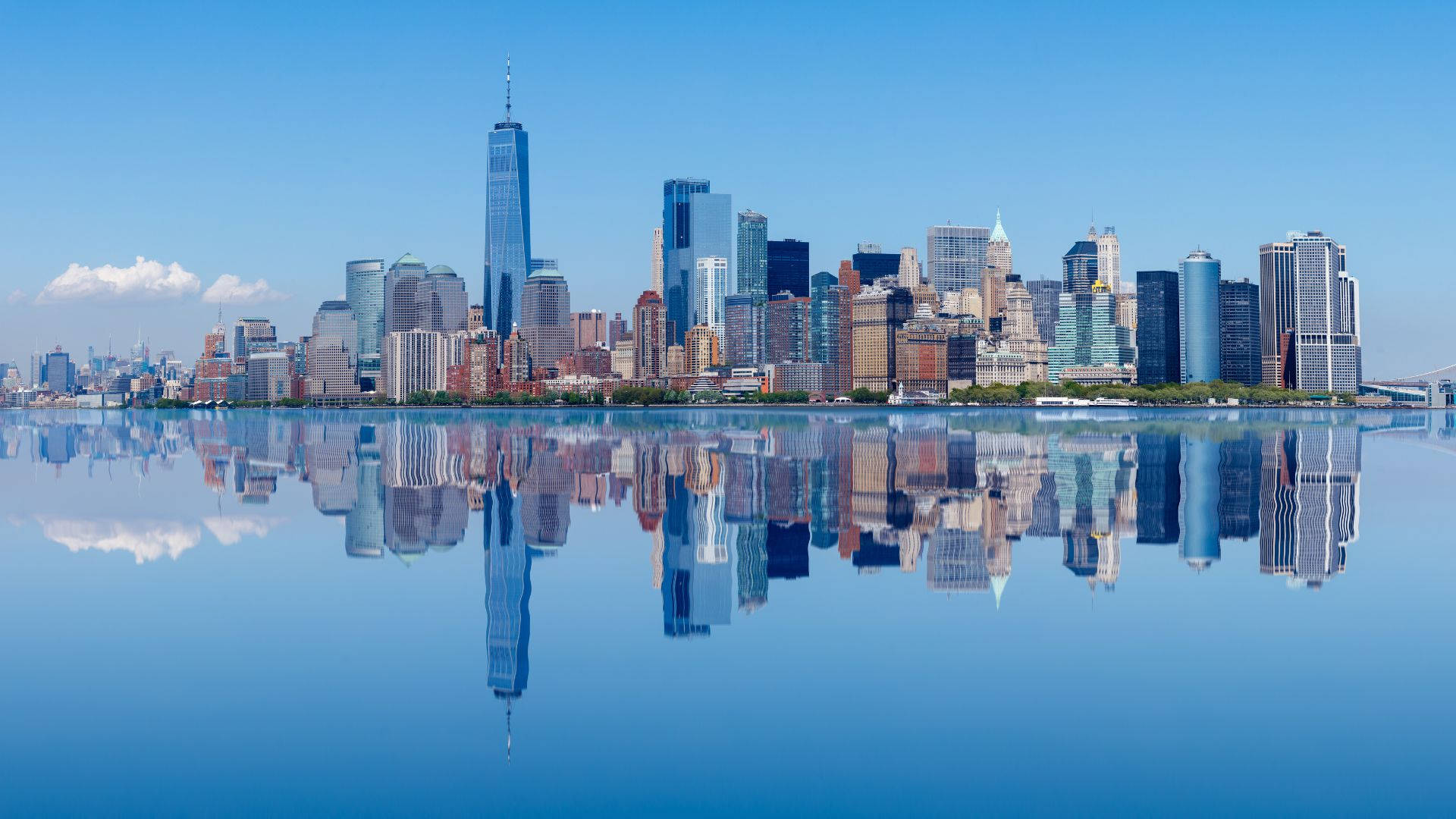 New York Skyline 桌布 壁紙 — 在晴朗的天空下，摩天大樓完美地倒映在平靜的藍色水面上，呈現出令人驚嘆的城市天際線。