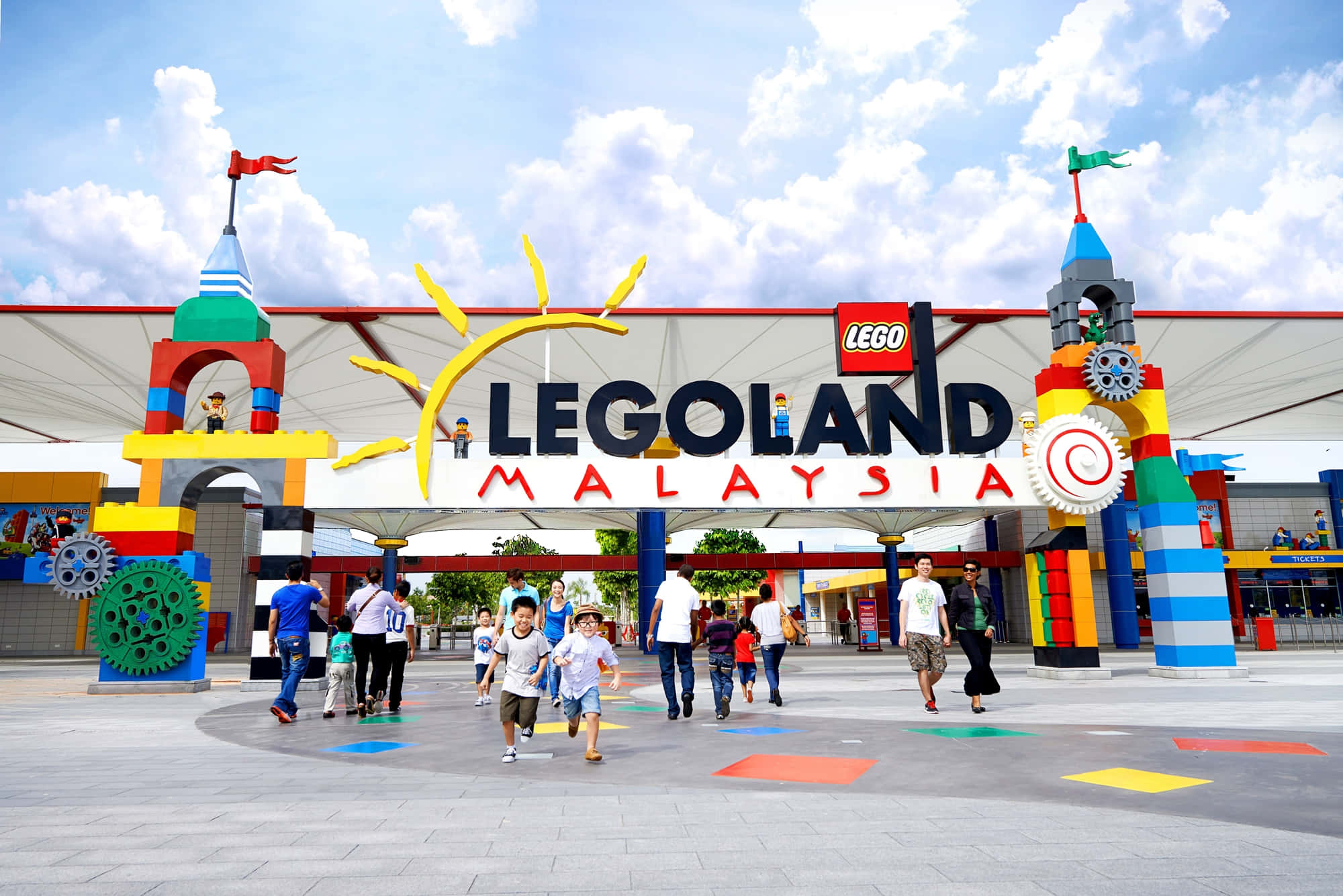 Legoland 桌布 壁紙 — 在晴朗的日子裡，孩子們和家庭在馬來西亞樂高樂園色彩繽紛的LEGO主題入口拱門下歡樂奔跑。
