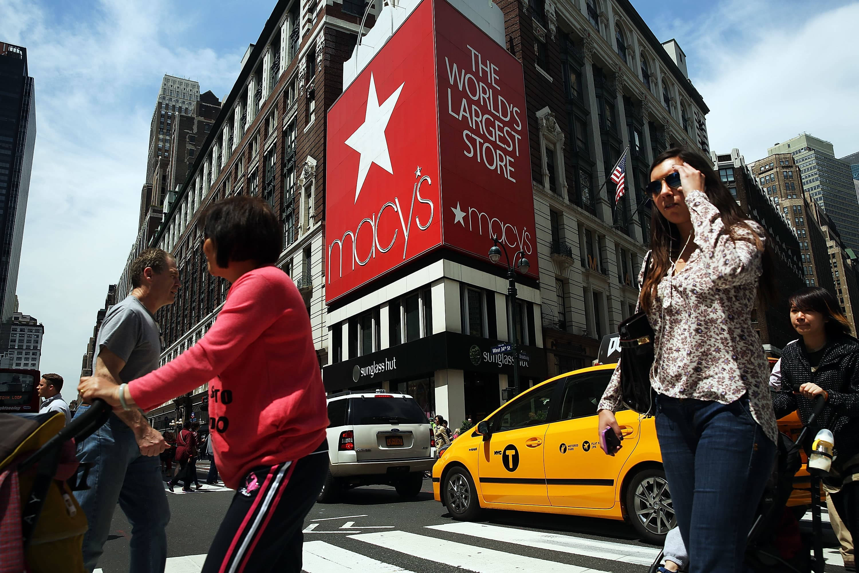 macys 桌布 壁紙 — 在晴朗的日子裡，行人穿過紐約繁忙的街道，下方是 Macy's 標誌性的紅星標誌。
