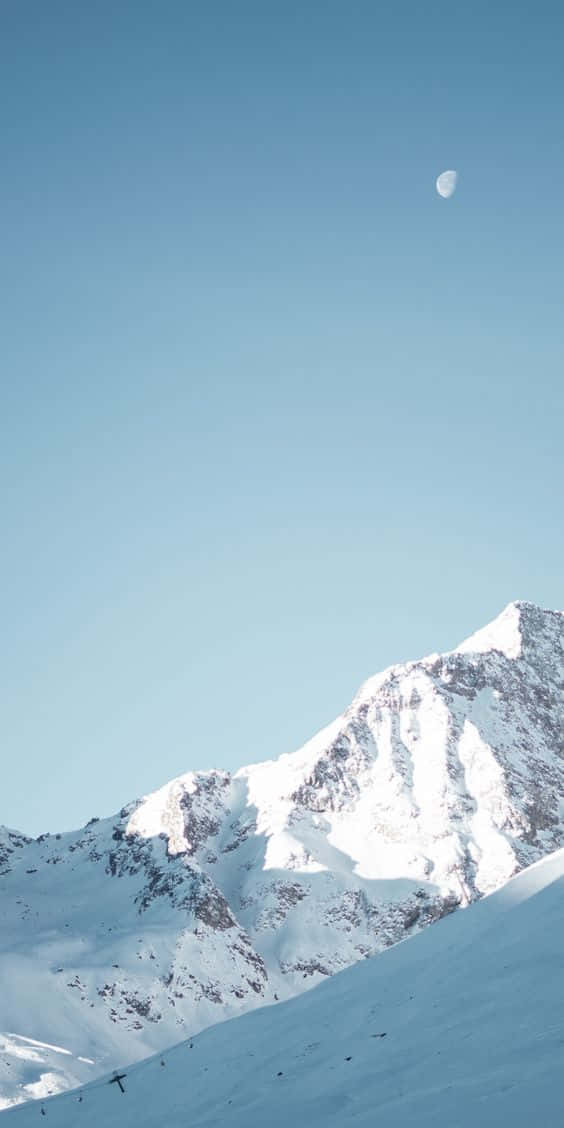 Snow iPhone 桌布 壁紙 — 在晴朗的藍天下，一座積雪的山峰寧靜地聳立，可見一彎新月。