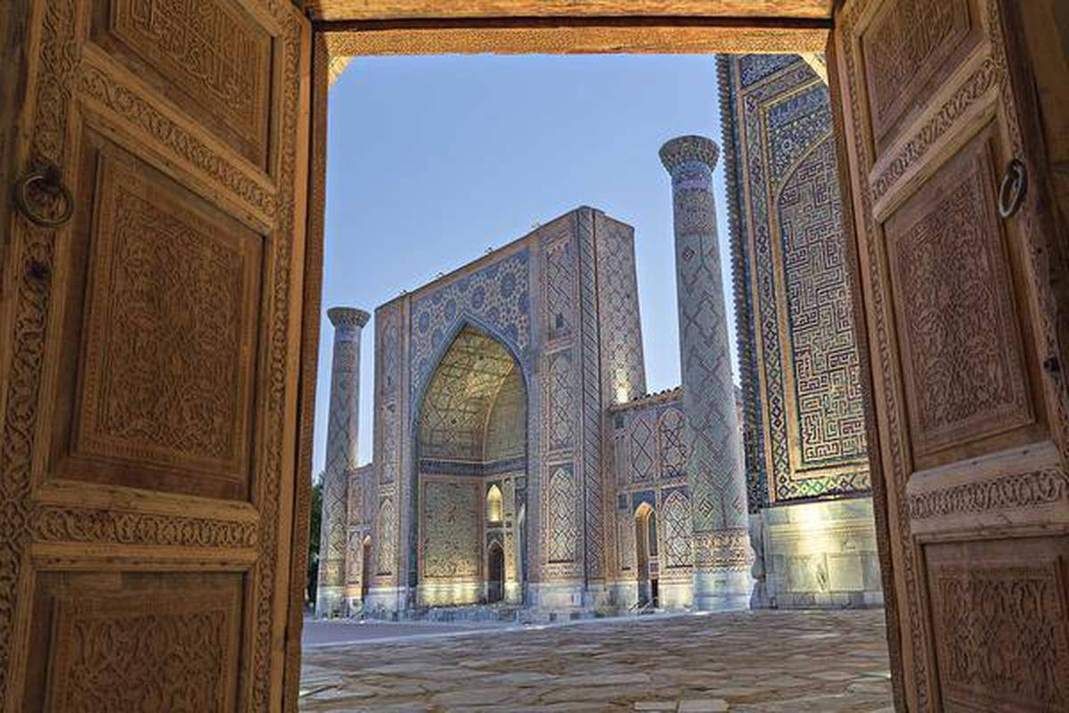 Uzbekistan 桌布 壁紙 — 在晴朗的藍天下，宏偉的伊斯蘭建築奇蹟被精雕細琢的木門框住。