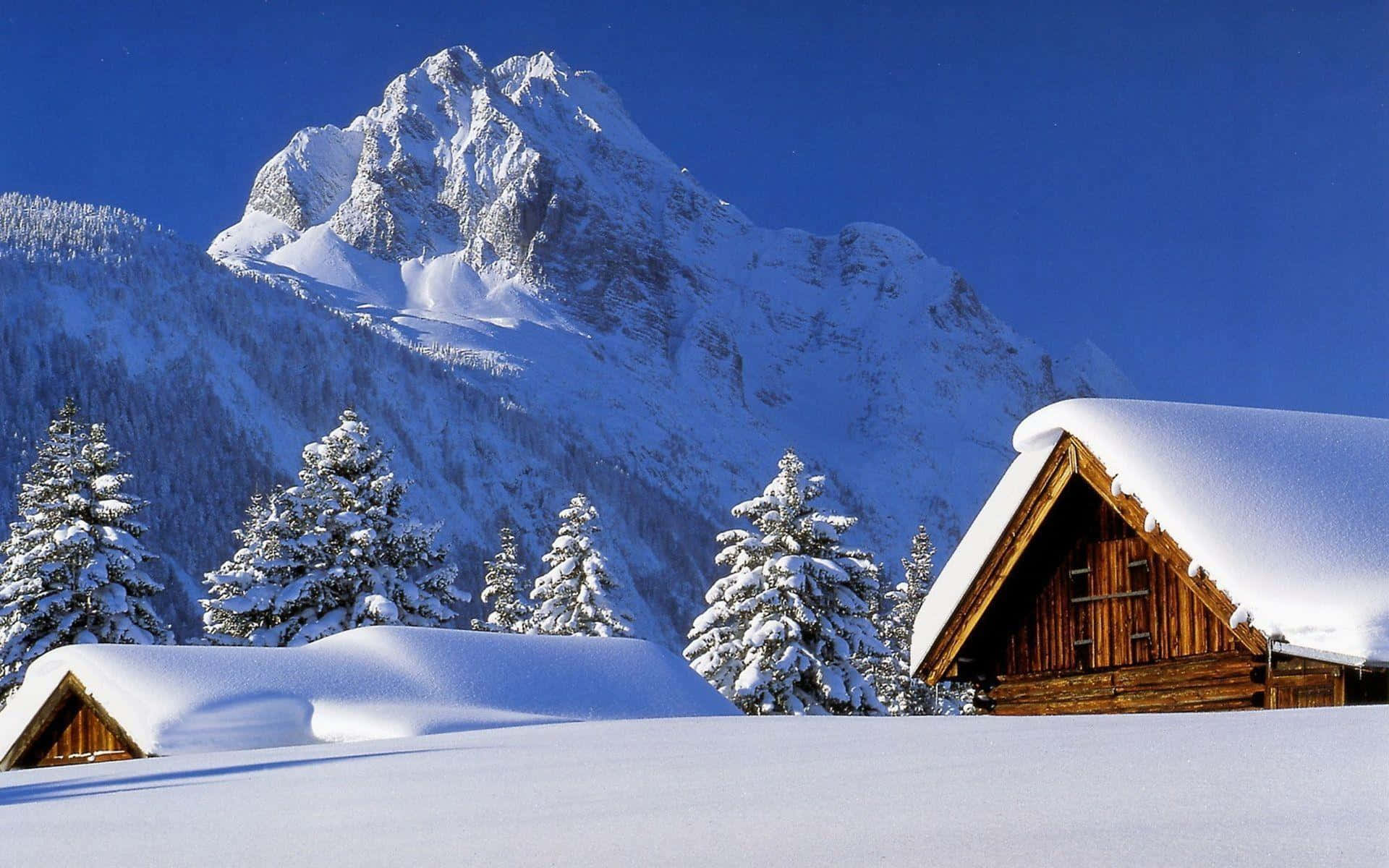 Winter Wonderland Desktop 桌布 壁紙 — 在晴朗的藍天下，寧靜的冬季山谷中，積雪覆蓋的木屋。