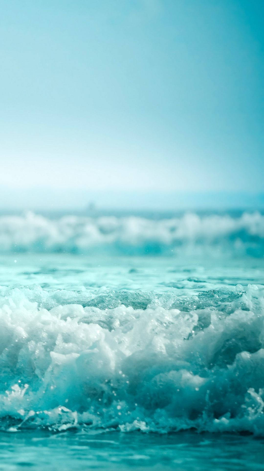 Ocean iPhone 桌布 壁紙 — 在晴朗的藍天下，平靜的海岸景色中，綠松石色的海浪拍打著白色泡沫。