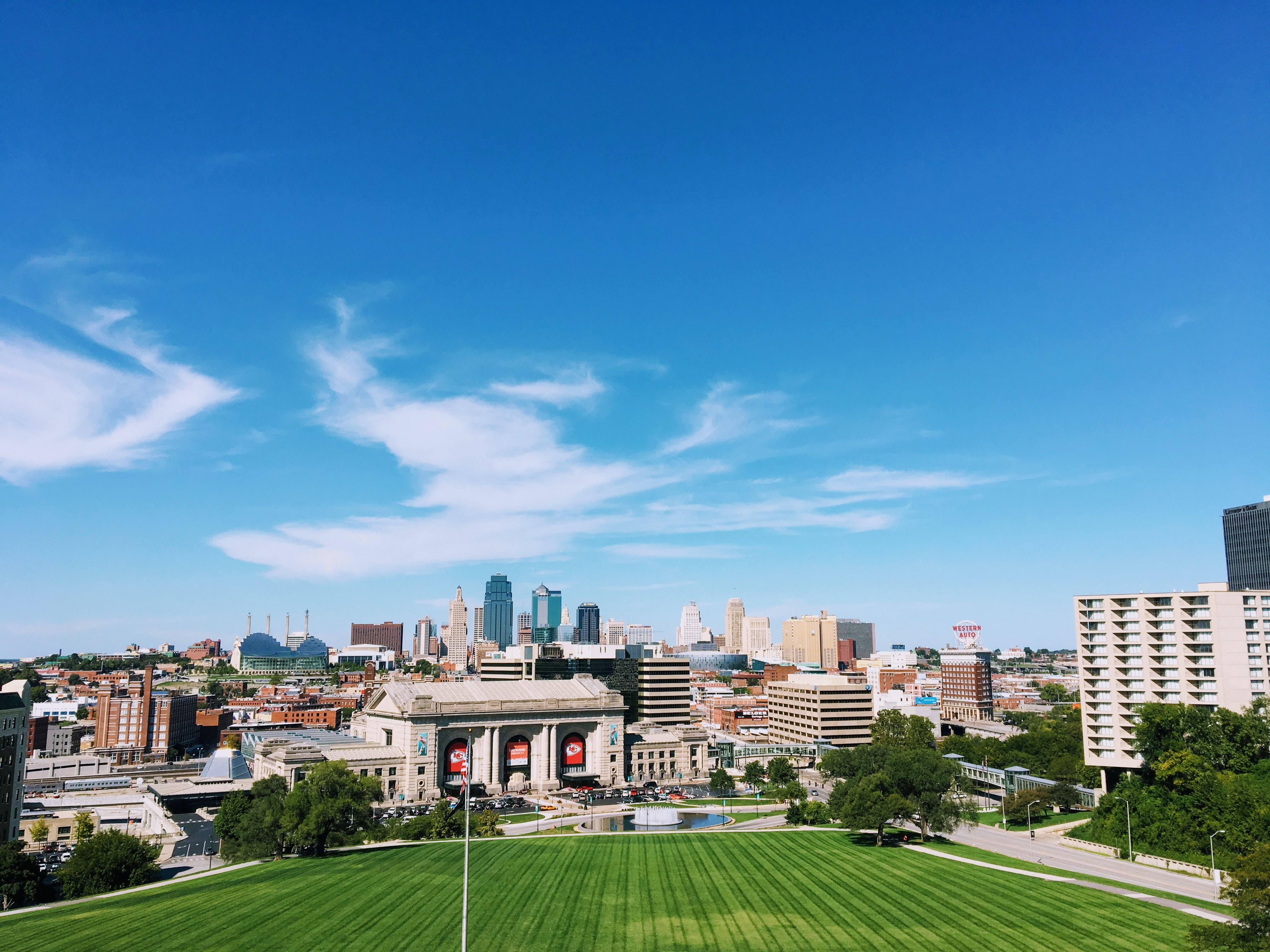 Kansas City 桌布 壁紙 — 在晴朗的藍天下，蓬鬆的白雲漂浮在鬱鬱蔥蔥的公園和歷史建築之上，充滿活力的城市景觀。