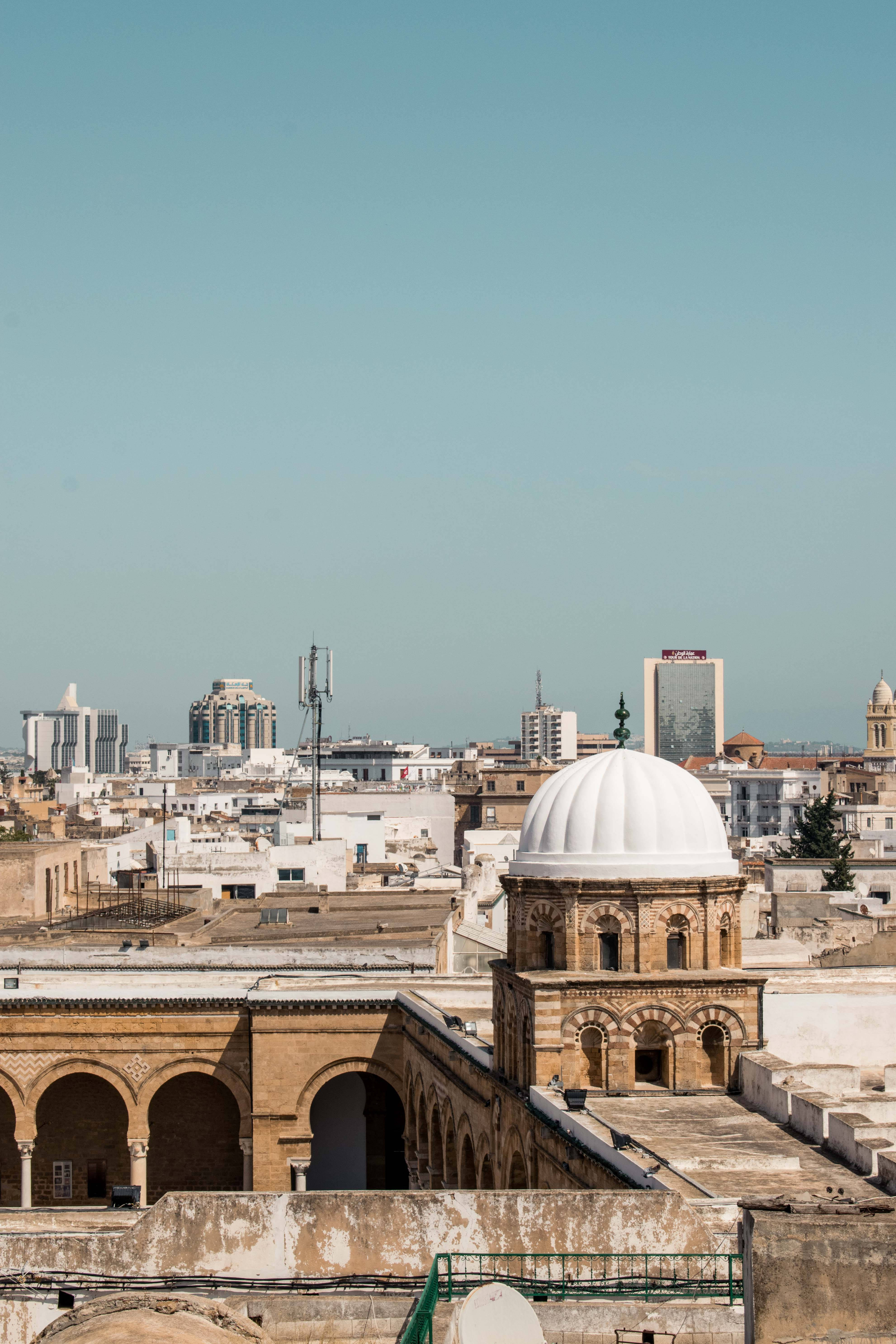 Tunisia 桌布 壁紙 — 在晴朗的藍天下，陽光普照的城市景觀融合了歷史圓頂建築與現代高樓大廈。