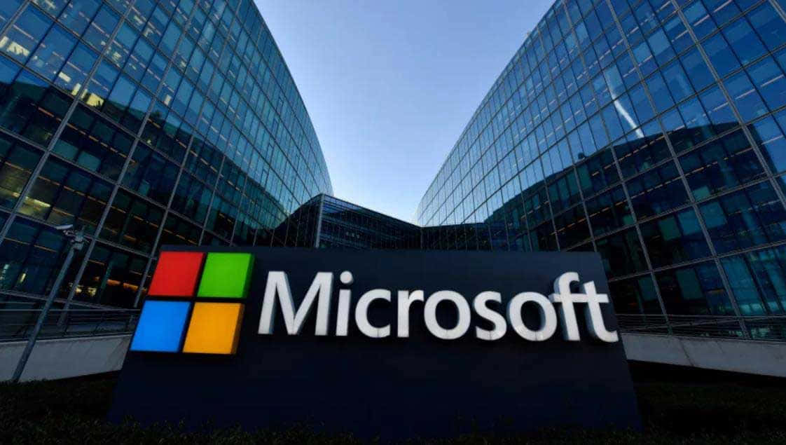 日落時分，玻璃辦公大樓前的Microsoft標誌牌。 — Microsoft 壁紙