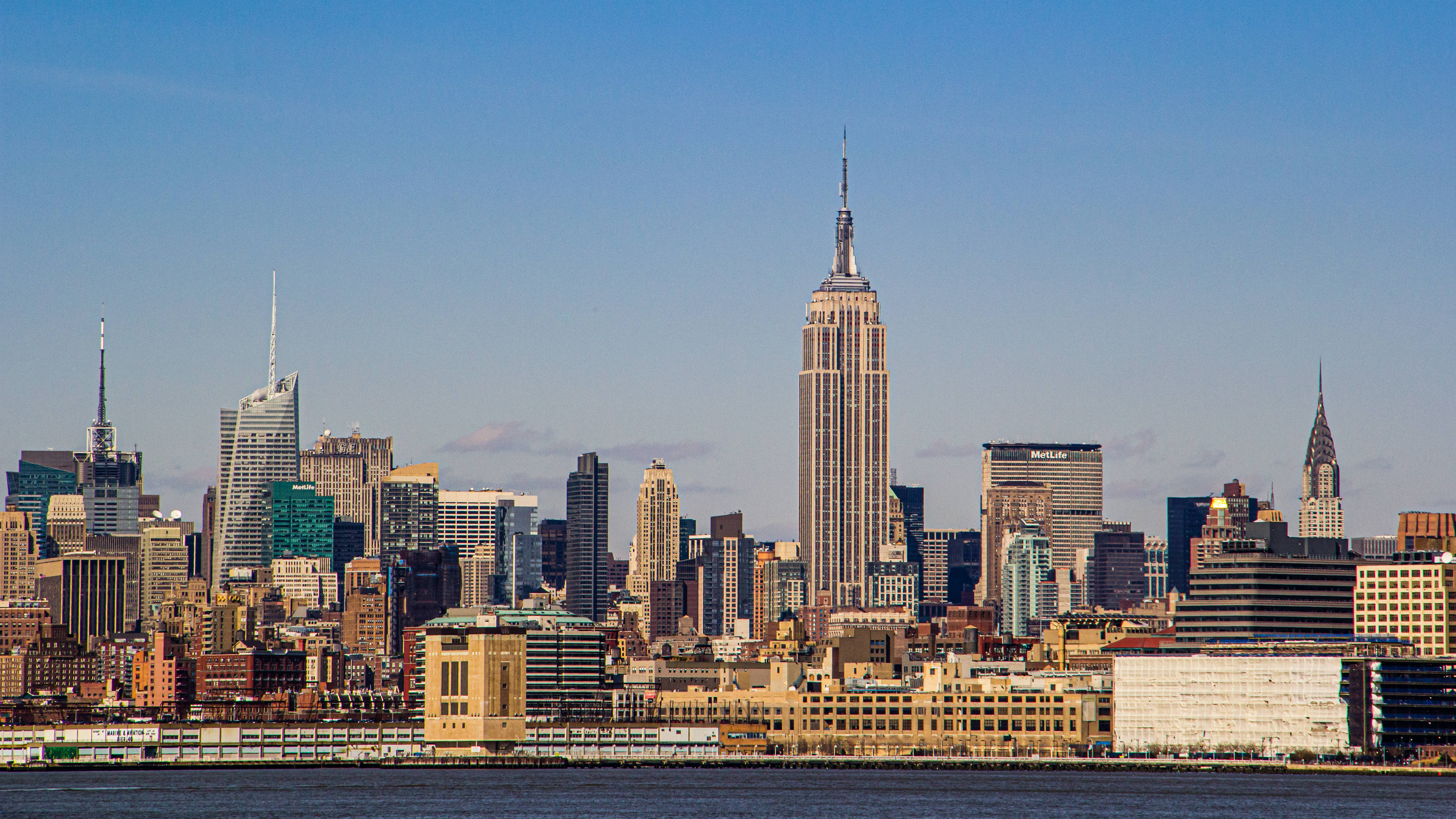 empire state 桌布 壁紙 — 在晴朗藍天下，帝國大廈聳立於現代摩天大樓之上的標誌性紐約市天際線。