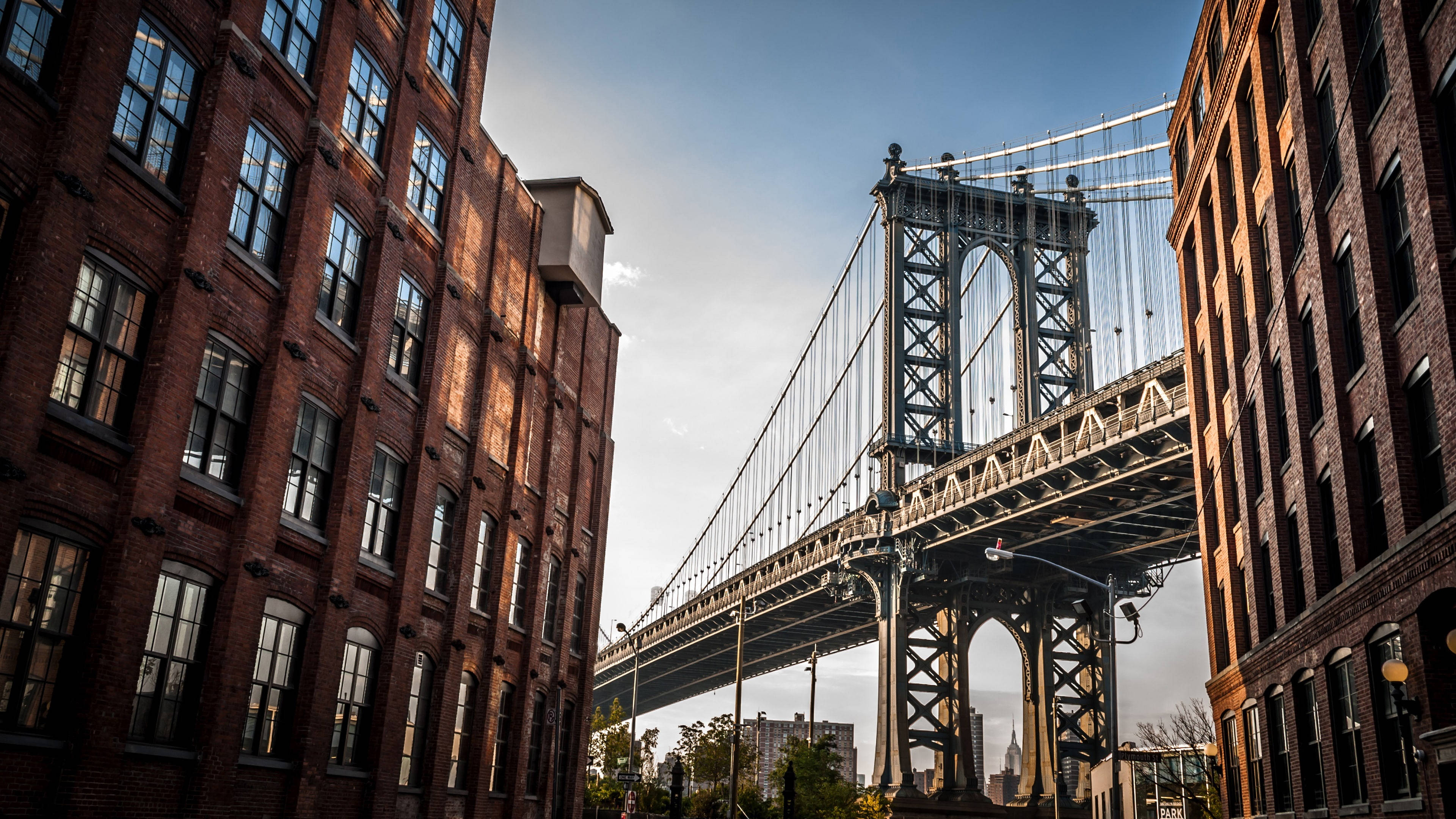 New York 桌布 壁紙 — 在晴朗藍天下，由高聳磚造建築物框住的曼哈頓大橋低角度景觀。