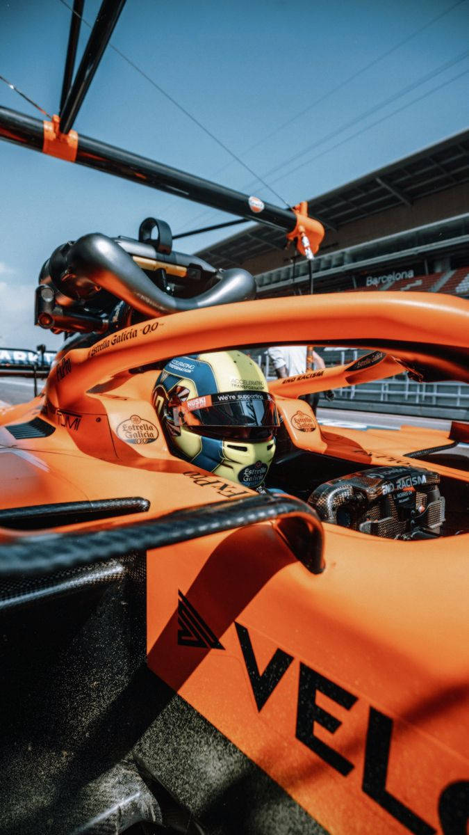 Formula 1 iPhone 桌布 壁紙 — 在晴朗藍天下，賽道上橙色麥拿侖F1賽車的車手特寫。