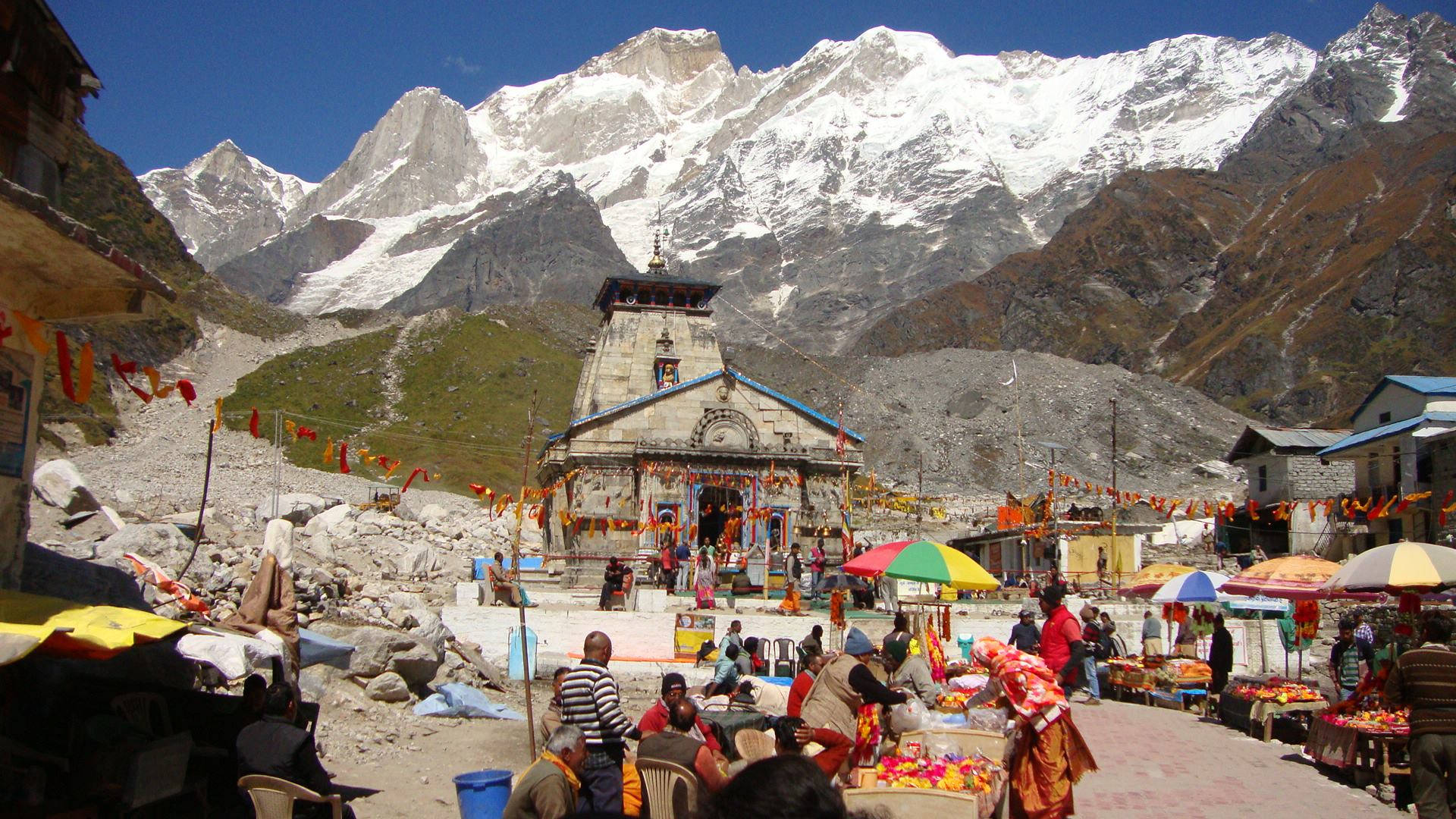 Kedarnath 桌布 壁紙 — 在晴朗藍天下，高聳的雪山山腳下，一個熱鬧的山村市集蓬勃發展。