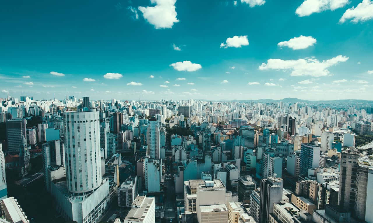 1280x768 桌布 壁紙 — 在晴朗藍天和 fluffy 白雲點綴下的現代城市景觀鳥瞰圖。
