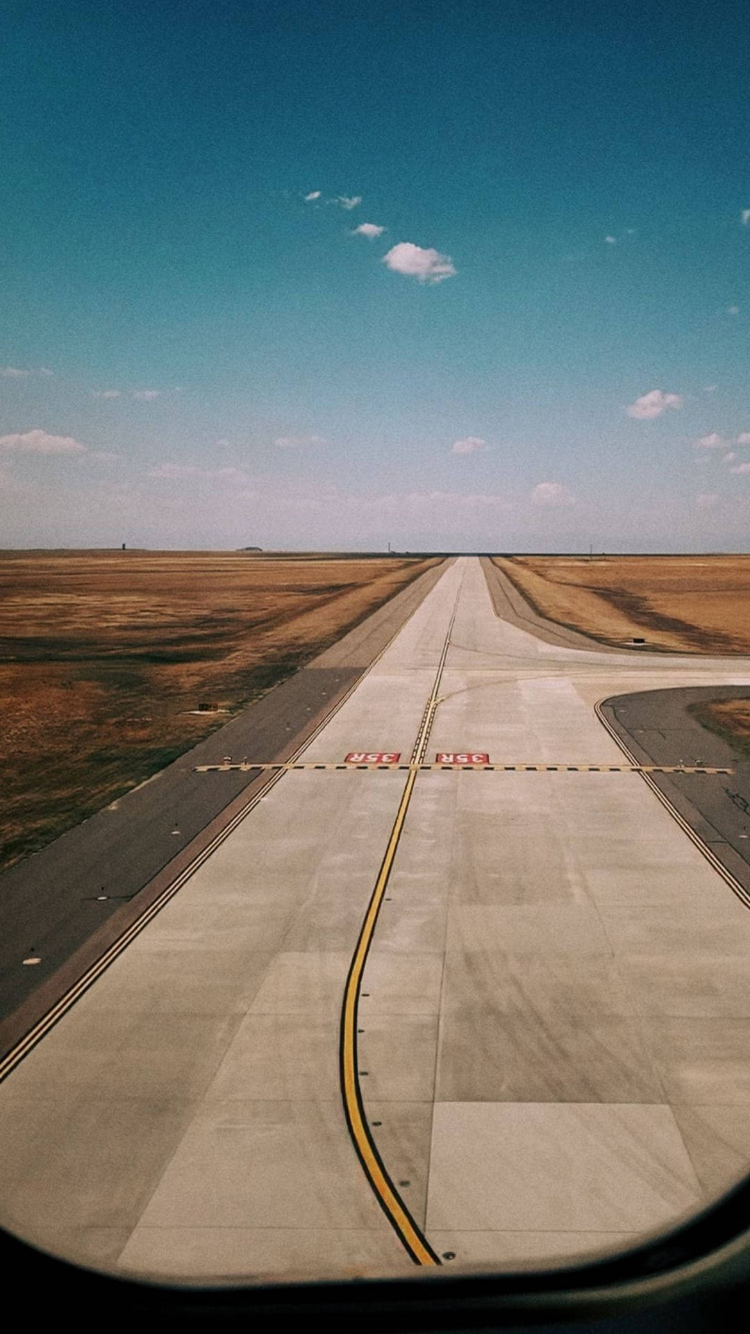 Runway 桌布 壁紙 — 在晴朗藍天和零星雲朵下，一條長長的機場跑道延伸至地平線的鳥瞰圖。